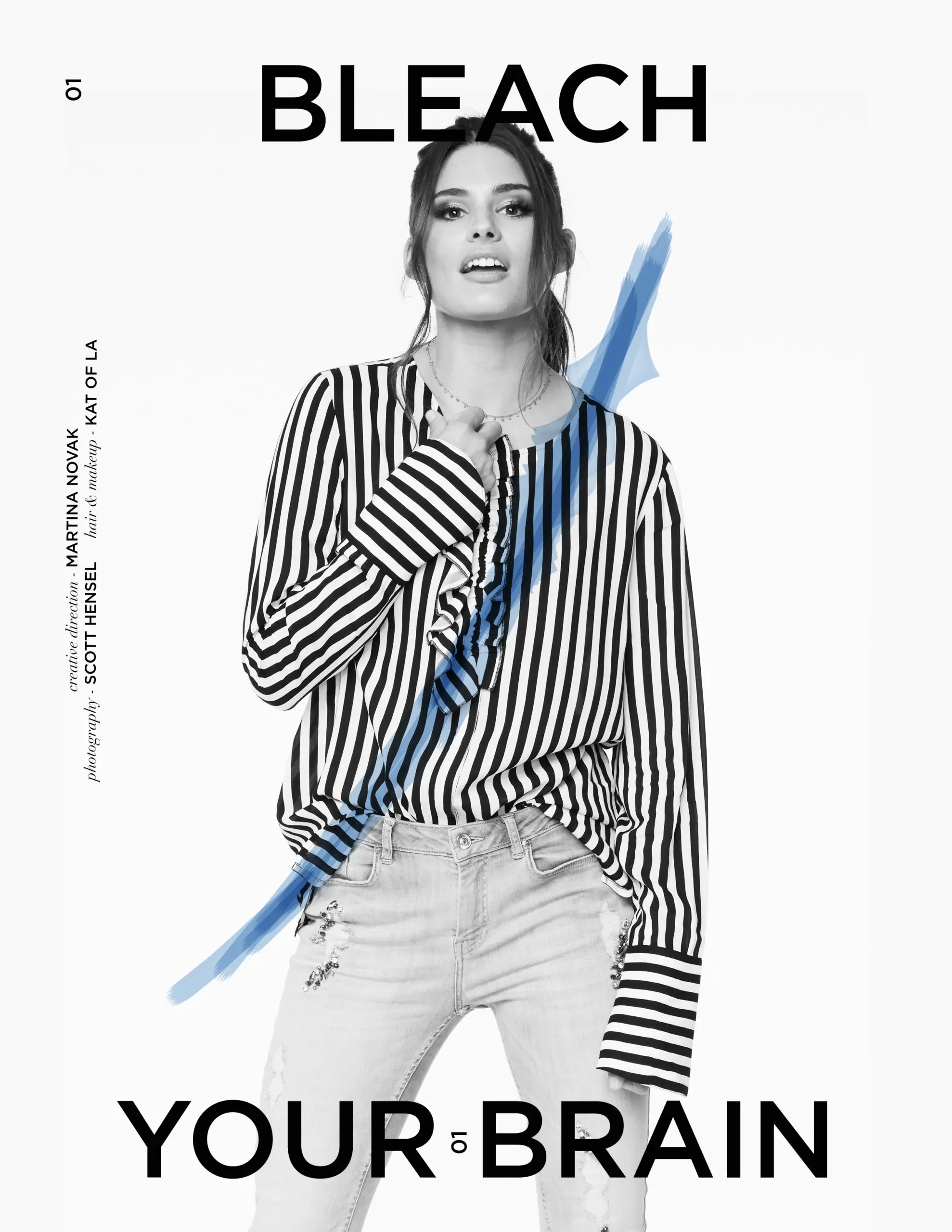 Woman wearing a black and white vertical striped blouse and light-washed ripped jeans, posing with one hand near her collar.