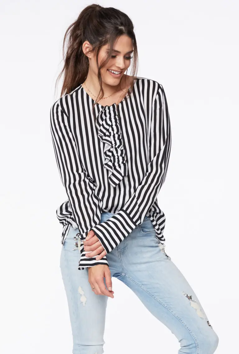 Smiling woman with long dark hair in a ponytail wearing a black and white vertical striped blouse with ruffle detail and light blue ripped jeans.