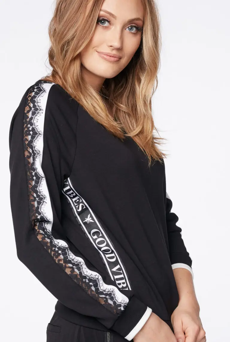 Woman wearing a black long-sleeve shirt with white lace stripes and the text 'GOOD VIBES' on the sleeve.