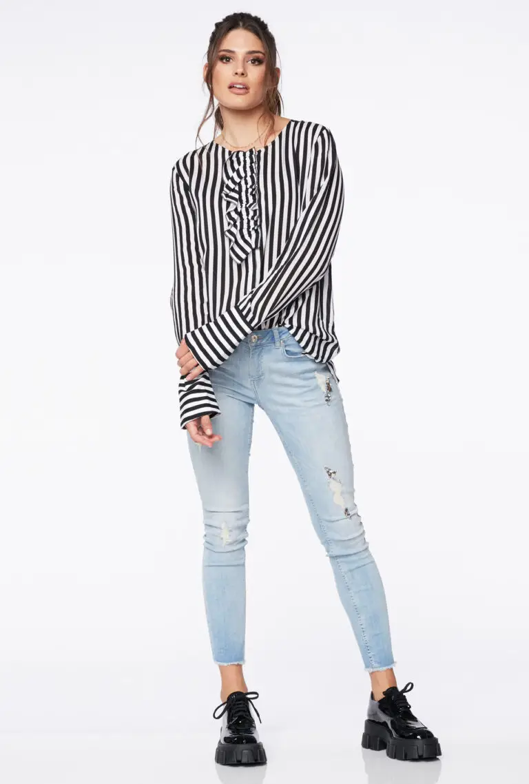 Woman wearing black and white vertical striped blouse with ruffles, light blue ripped skinny jeans, and black chunky platform shoes.