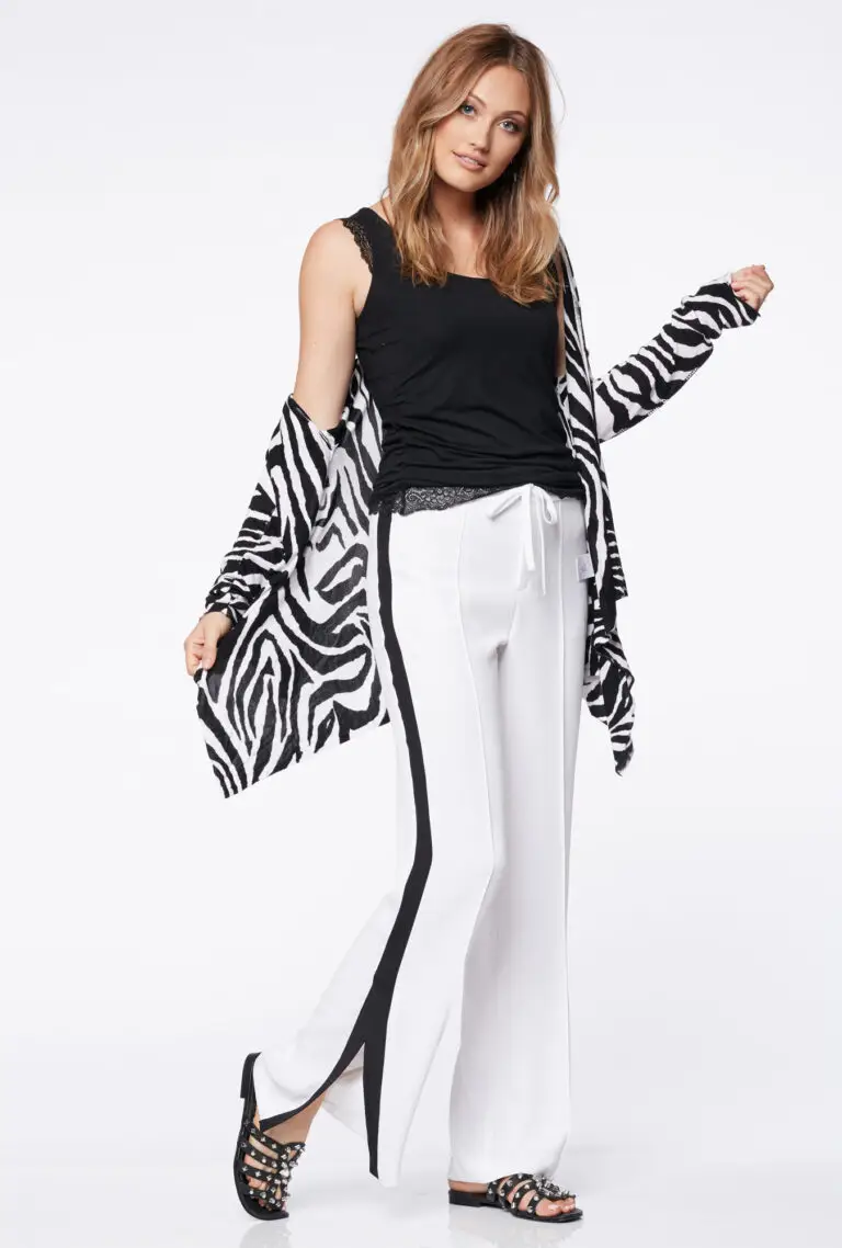 Woman wearing white pants with black side stripes, black lace-trimmed tank top, zebra print cardigan, and black studded sandals.