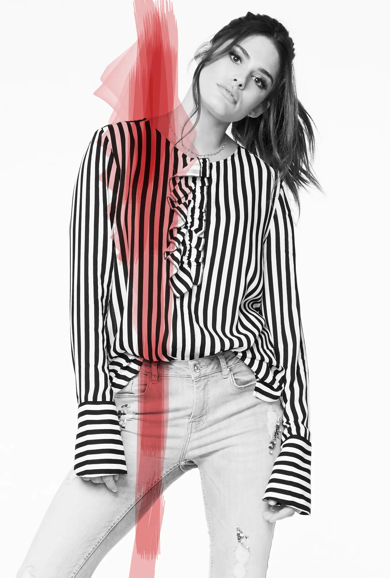 Woman wearing a black and white vertical striped blouse with ruffle detail and light ripped jeans, posing against a white background with a red paint streak overlay.