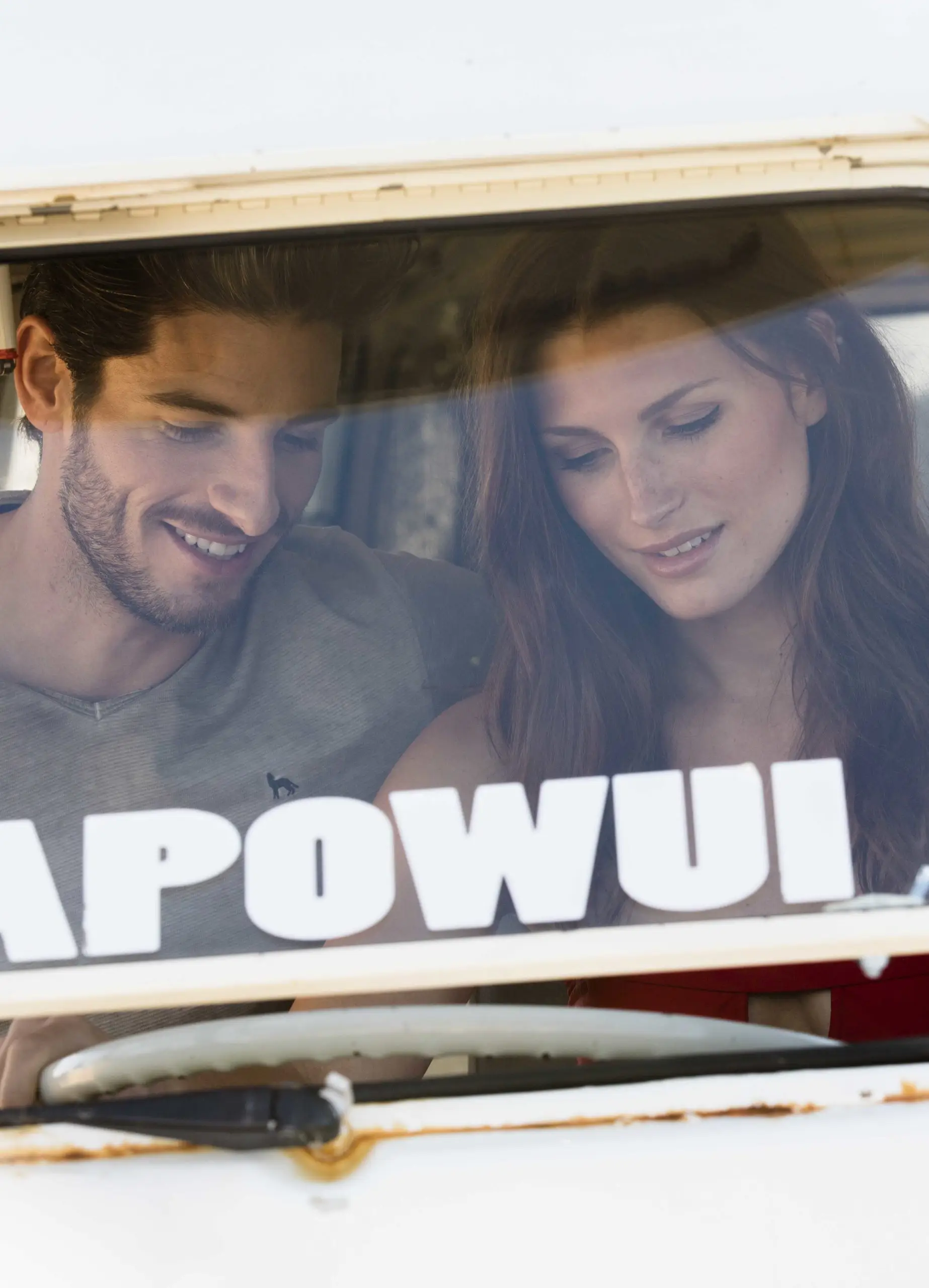 Young man and woman smiling and looking down inside a vehicle through the windshield.