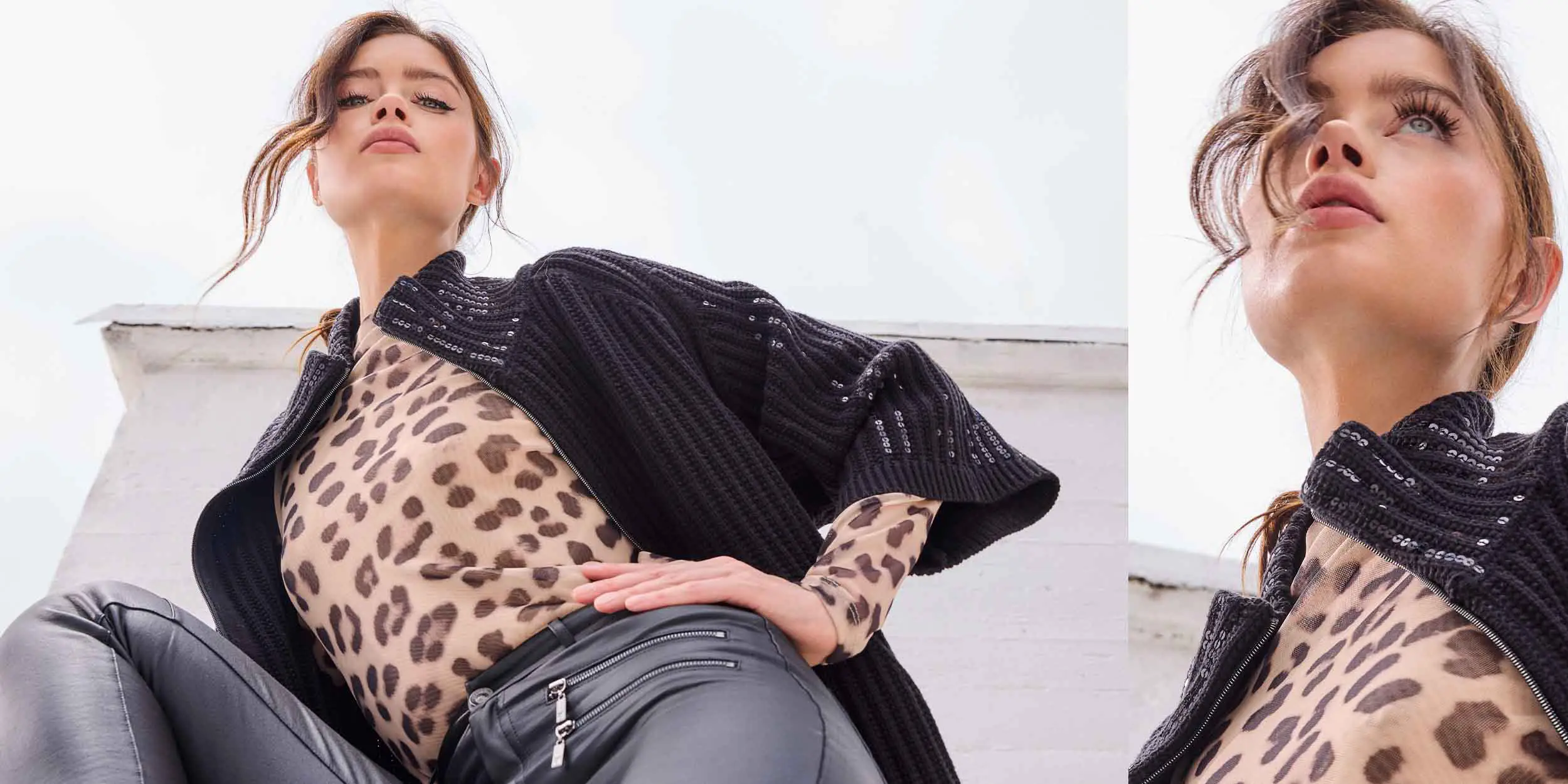 Low-angle view of a woman wearing a black knitted jacket over a leopard print top and black leather pants, posing against a white wall.