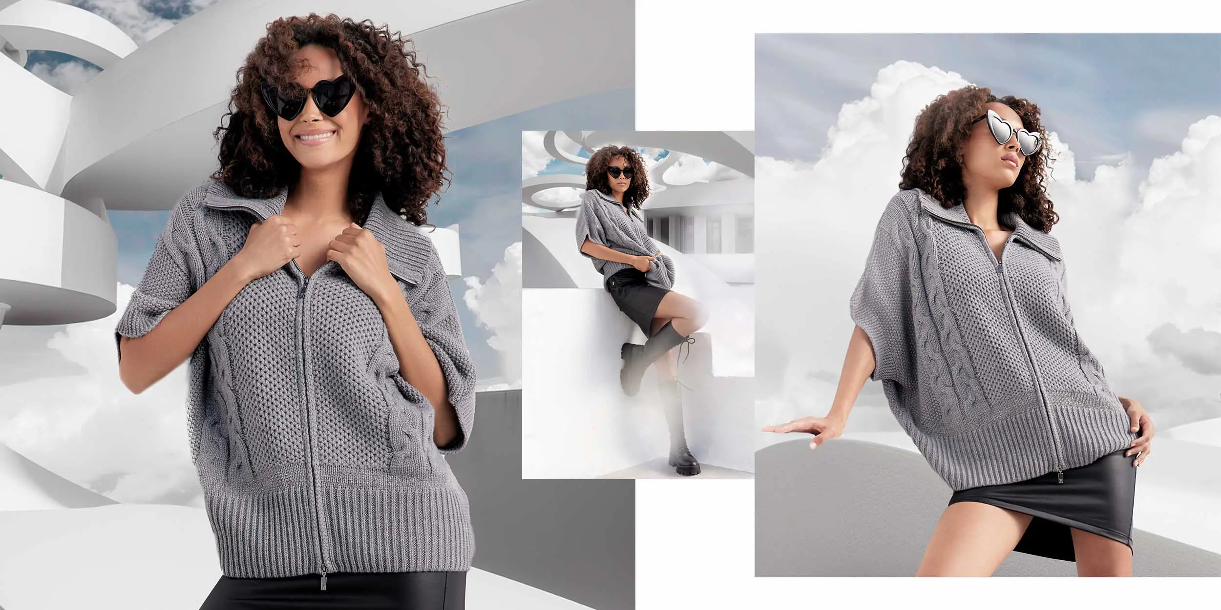 Woman with curly hair wearing heart-shaped sunglasses and a gray knit zip-up sweater over a black skirt, posing against a modern white architectural background with clouds.