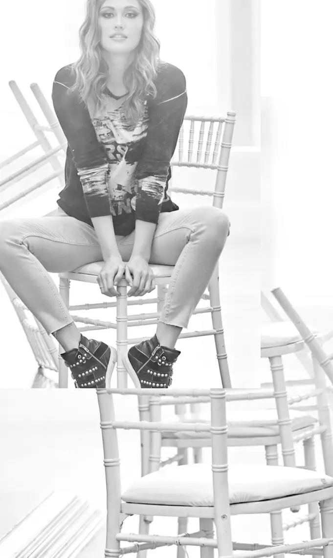 Woman sitting on a wooden chair, wearing a casual sweatshirt, jeans, and studded ankle boots.