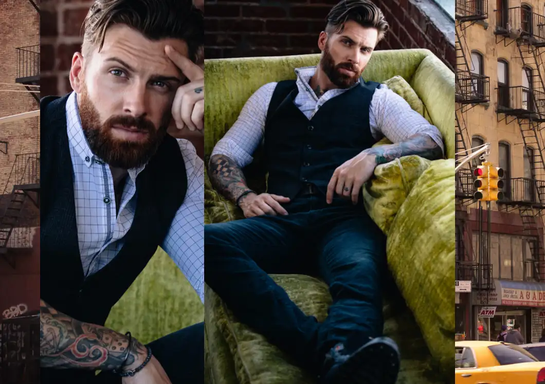 Bearded man with tattoos wearing a black vest and checkered shirt sitting on a green couch in an urban setting.