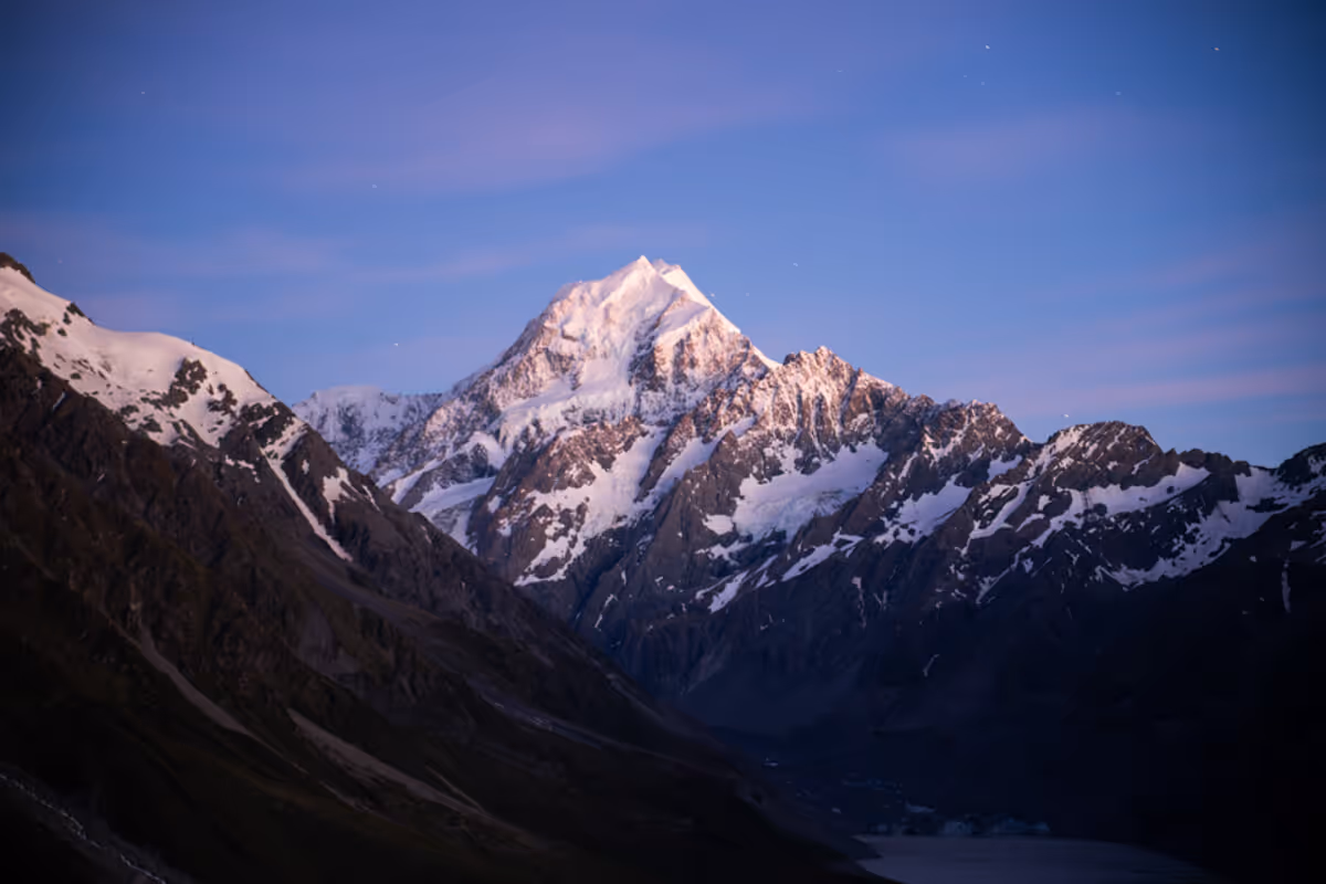 Snow-capped mountain peak at dusk with a clear purple and blue sky.