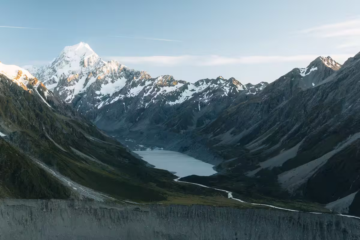 Snow-capped mountain range with a glacier-fed lake in the valley under a clear sky.