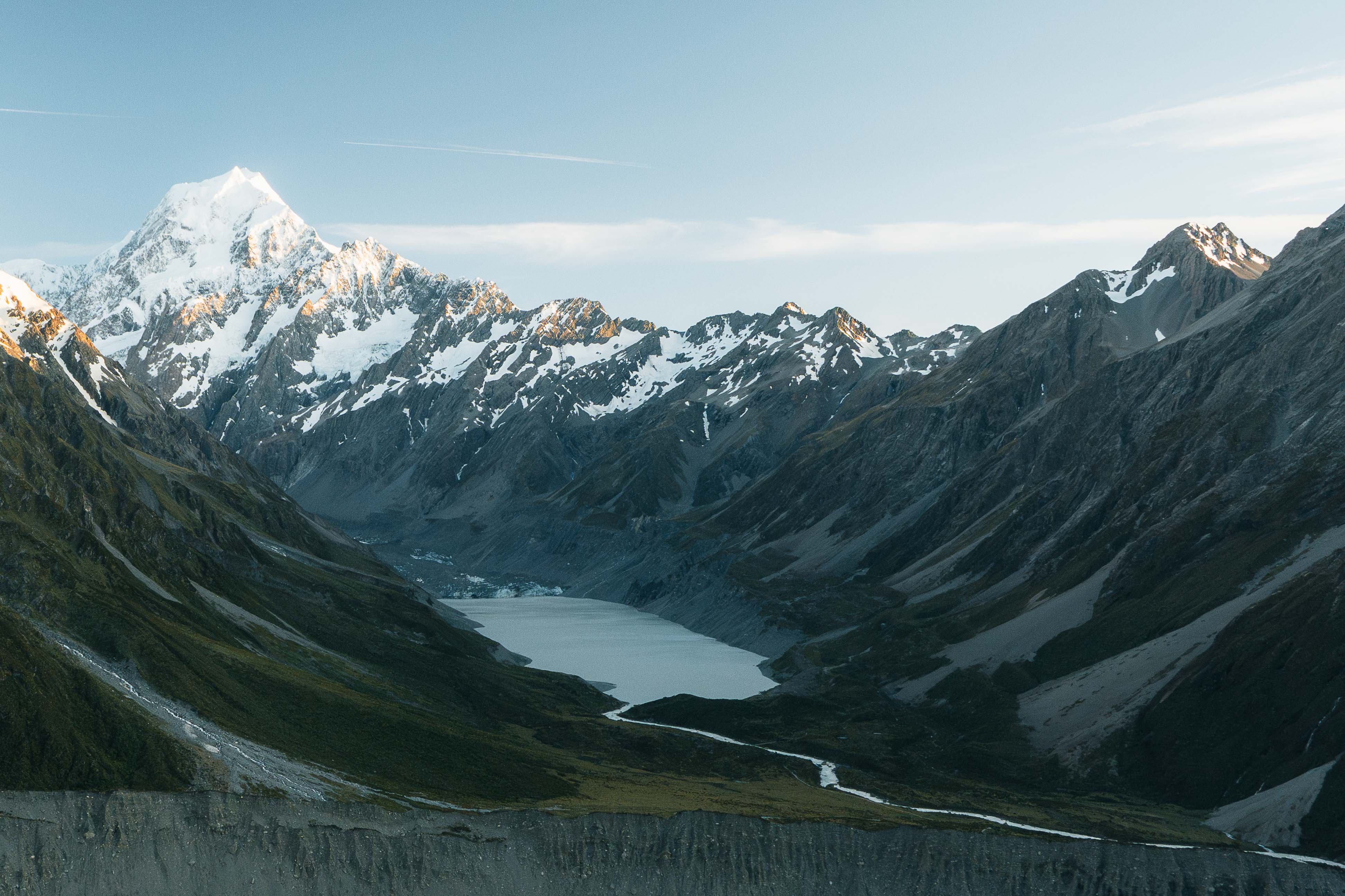Snow-capped mountain range with a glacier-fed lake in the valley under a clear sky.