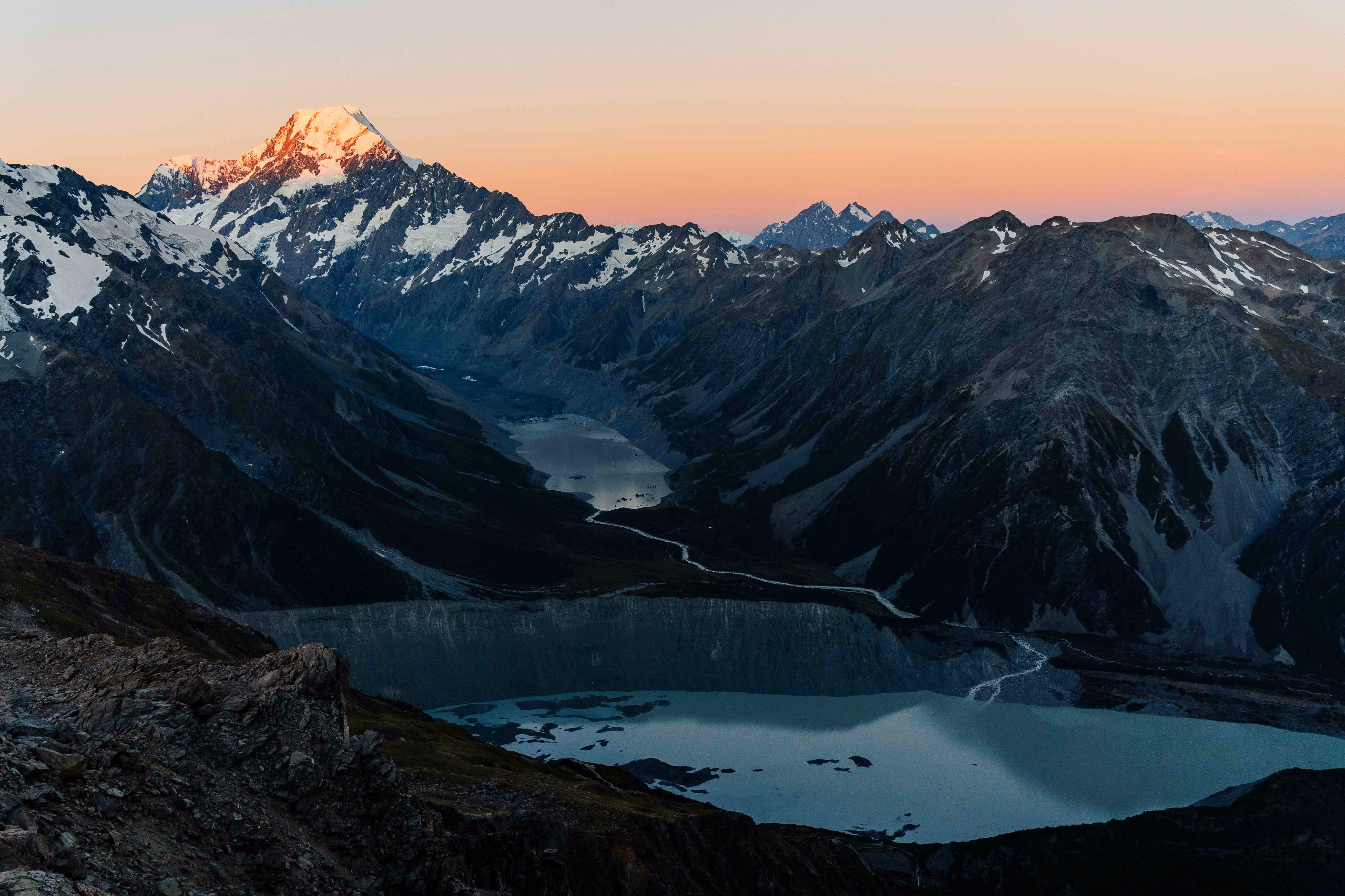 Mountain landscape at sunset with snow-capped peaks, a glacier, and two turquoise lakes in a valley.