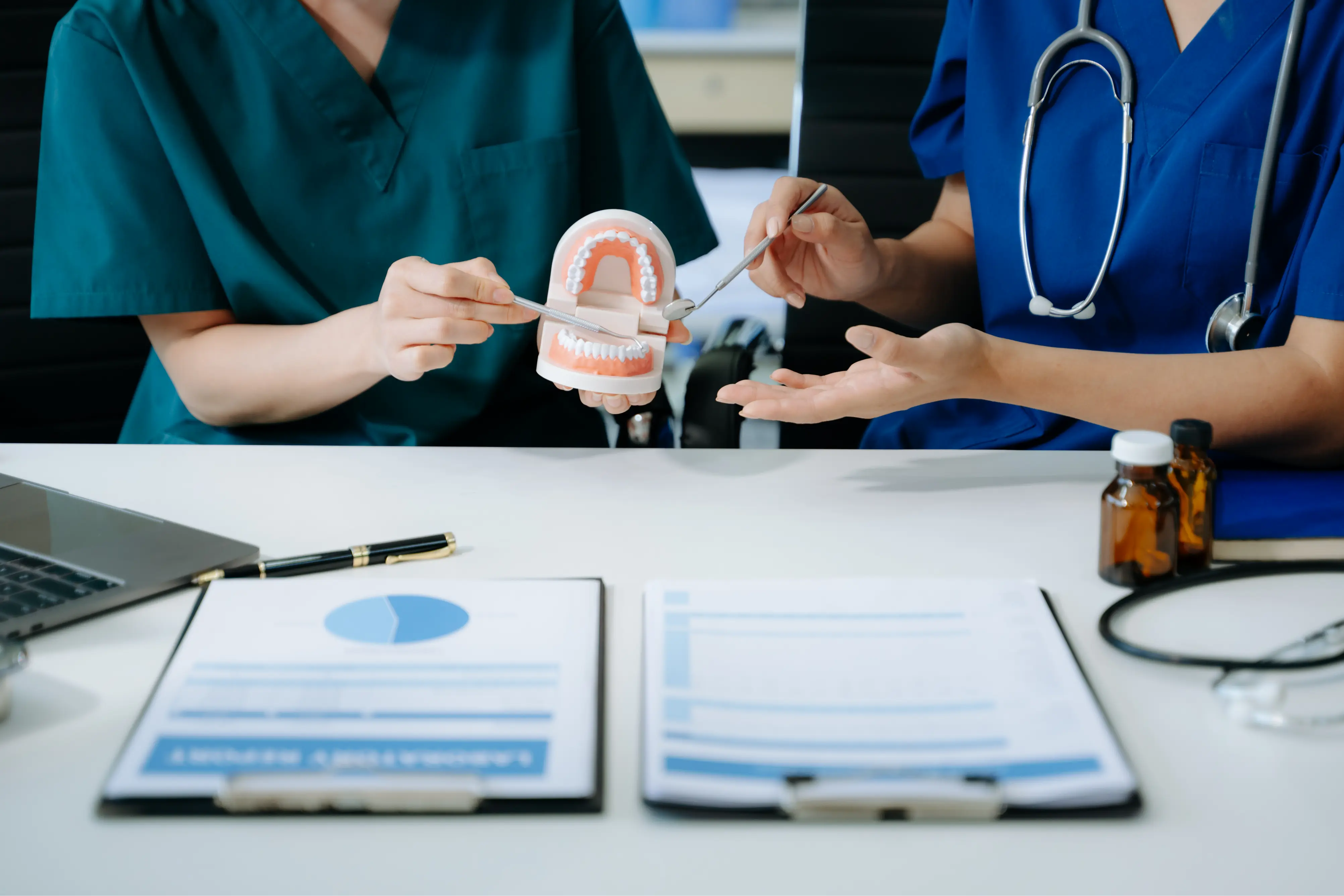 Team of dentists in scrubs reviewing documents and using a dental model to explain oral health plans and treatment options to a patient