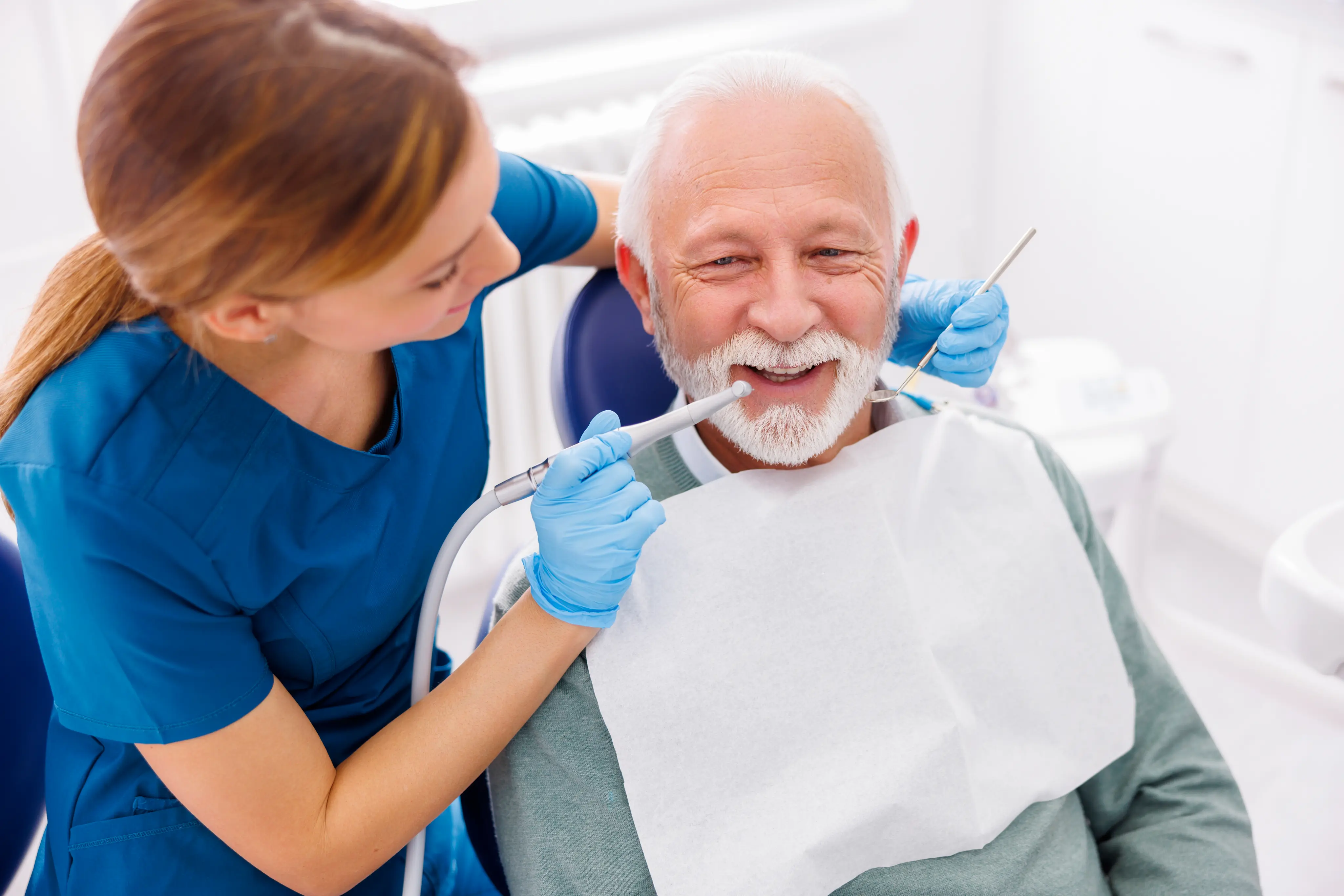 Smiling dentist showing an elderly male patient his dental results while discussing treatment options in a modern clinic representing compassionate senior dental care
