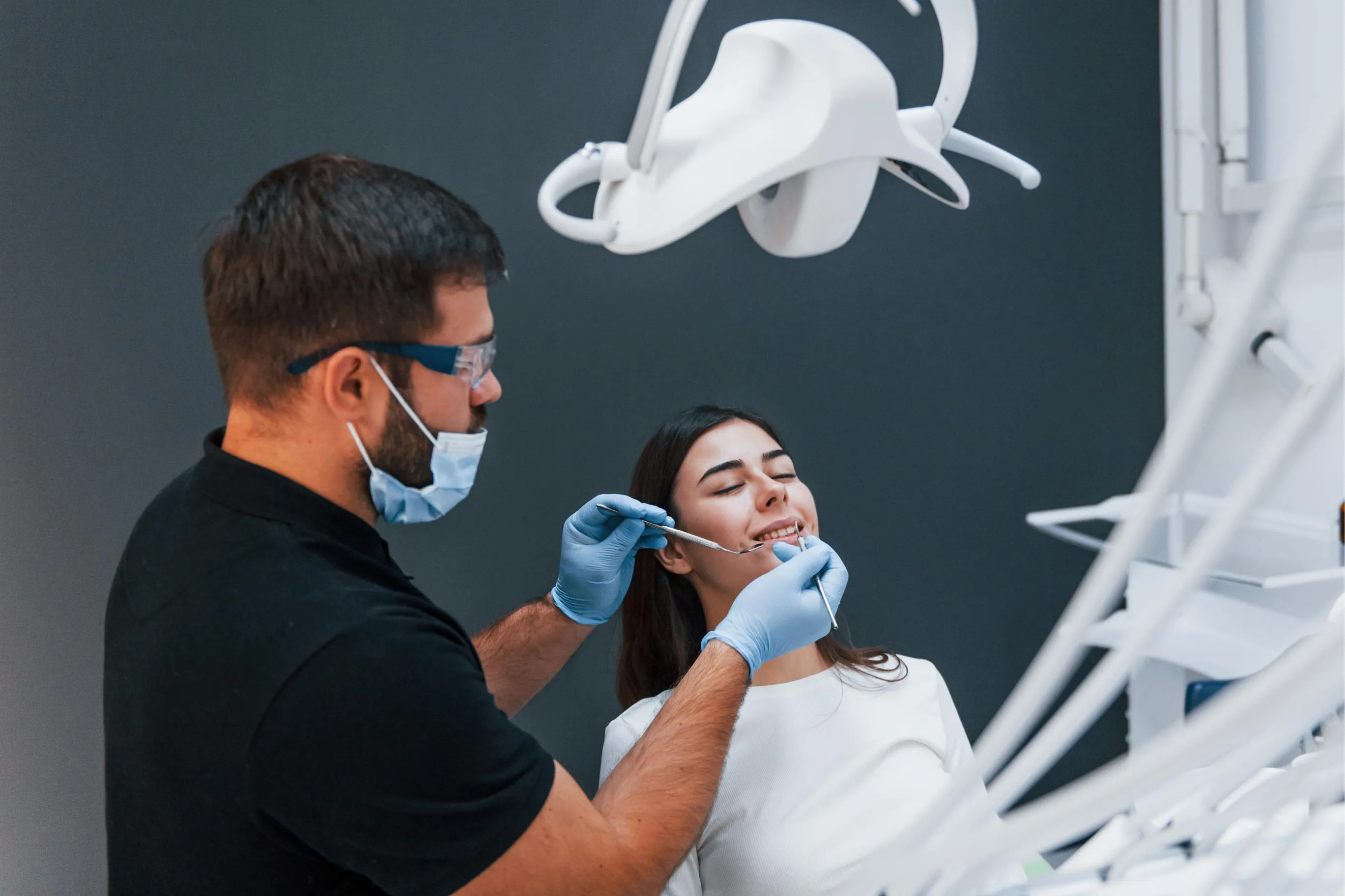 Dentist wearing protective mask and gloves consulting a smiling female patient seated in the dental chair during an orthodontic checkup