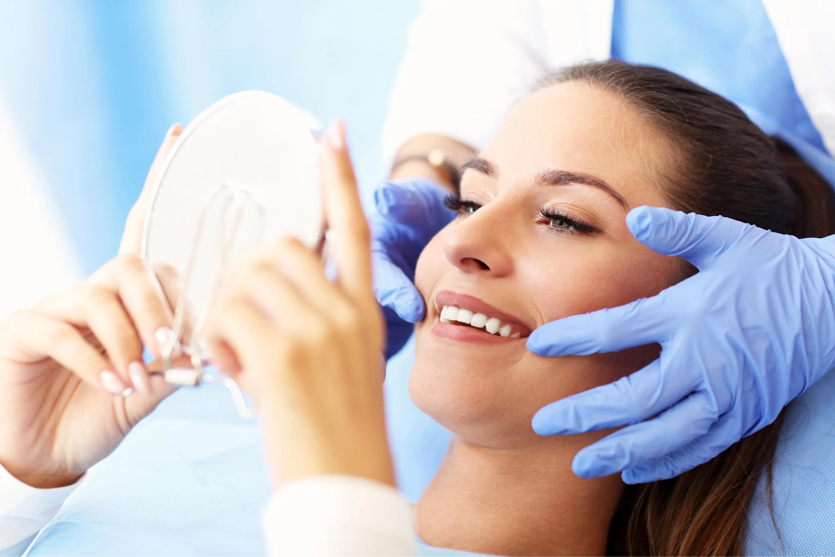 Dentist wearing blue gloves showing a female patient her results in a mirror after a professional teeth whitening procedure emphasizing patient satisfaction