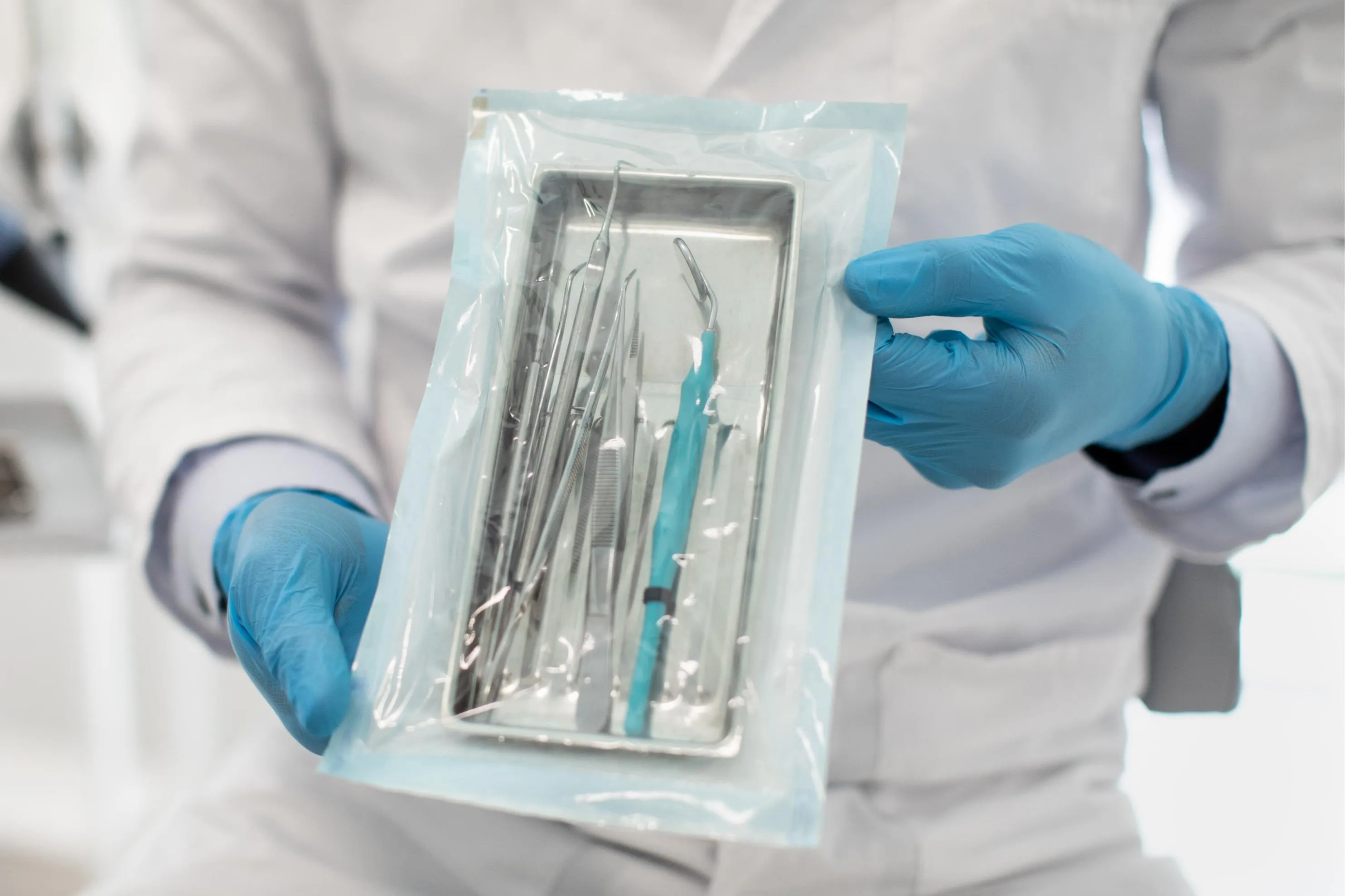 Dentist wearing blue gloves holding a sealed sterilization pouch containing dental instruments ensuring proper hygiene and infection control in the clinic