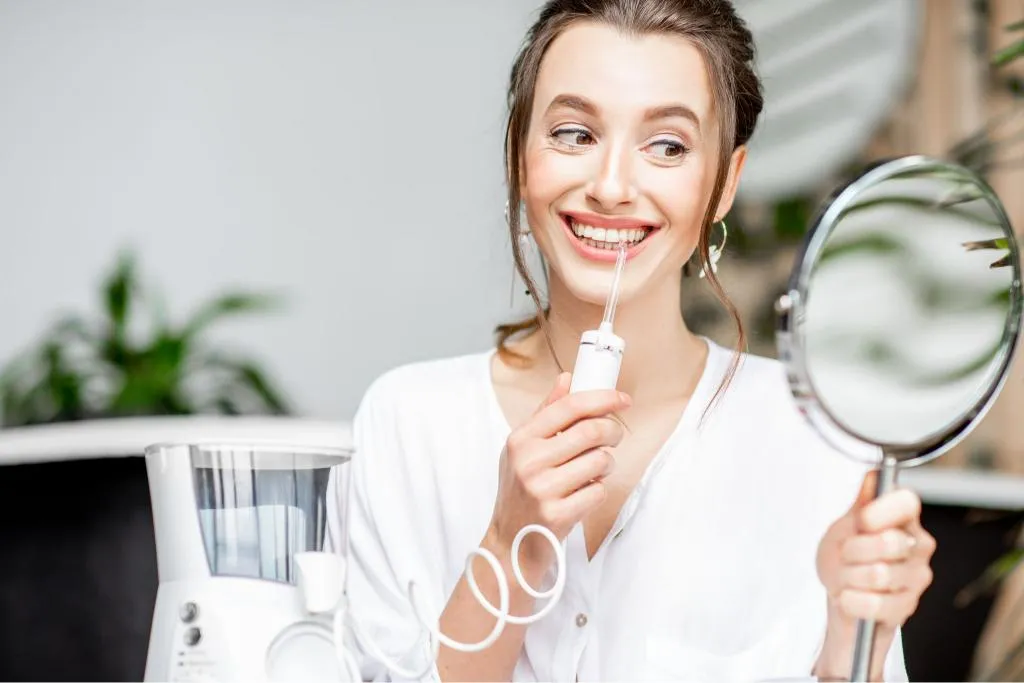 Smiling woman holding a toothbrush and looking into a mirror representing good oral hygiene habits and satisfaction with professional dental care results