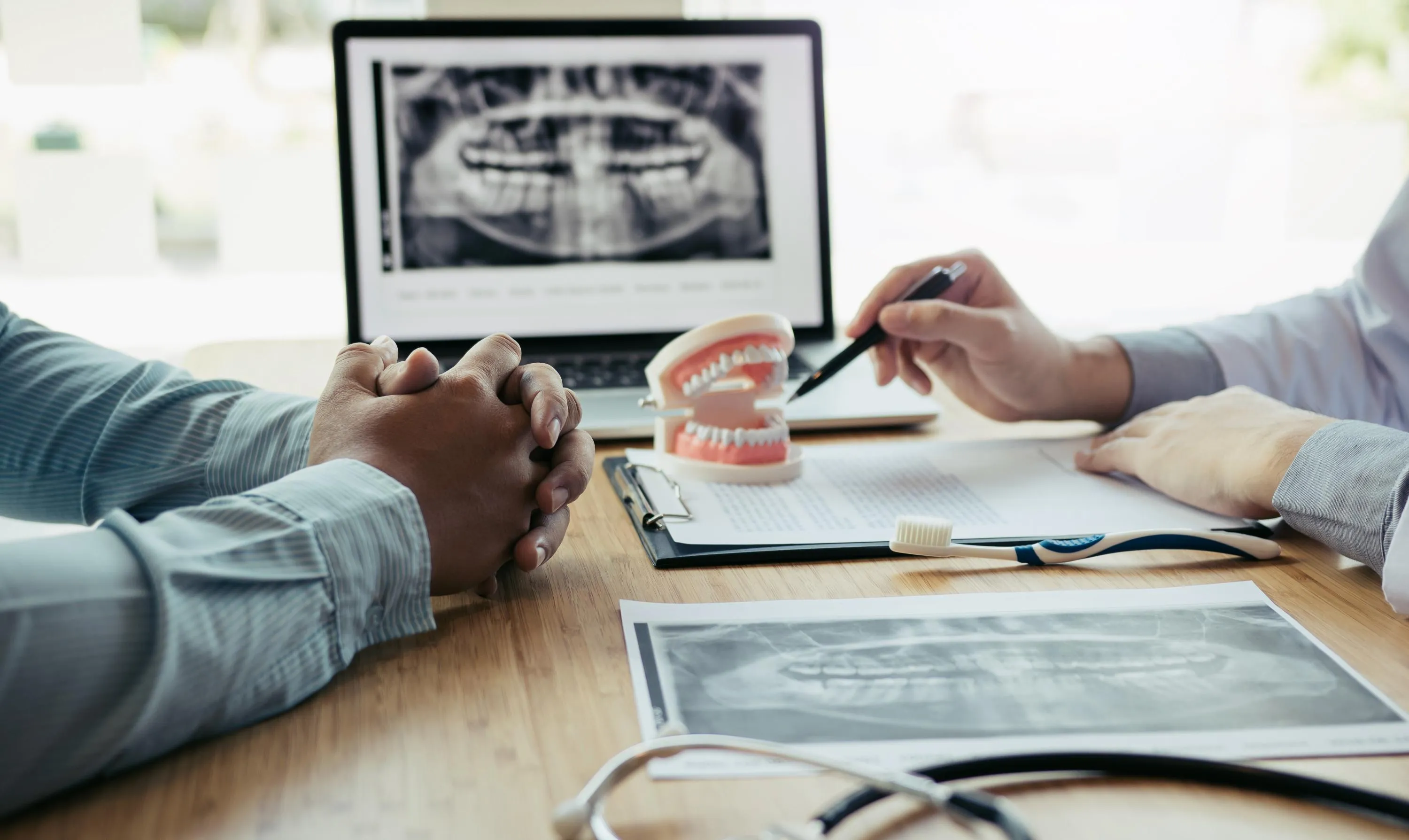 Dentist showing a patient’s panoramic dental X-ray on a tablet while explaining treatment options and demonstrating tooth structure using a model during consultation