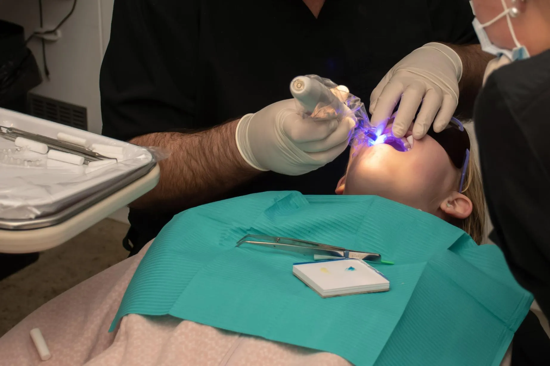 Dentist using a blue LED curing light to harden dental composite material while performing a restorative procedure on a patient reclined in the dental chair