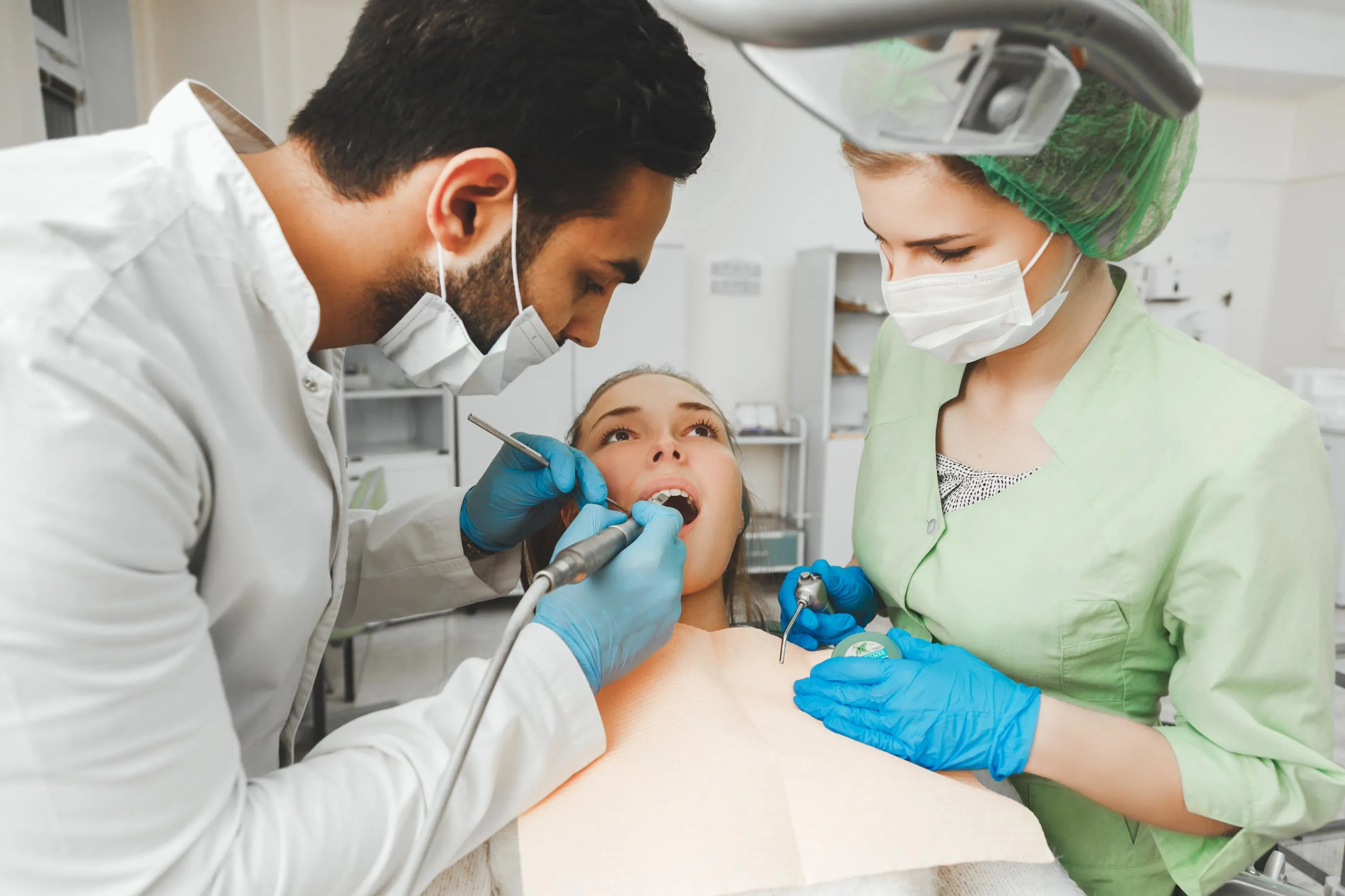 Dentist and assistant in protective gear examining a young child in a pediatric dental clinic focusing on gentle, caring, and comfortable dental care for kids
