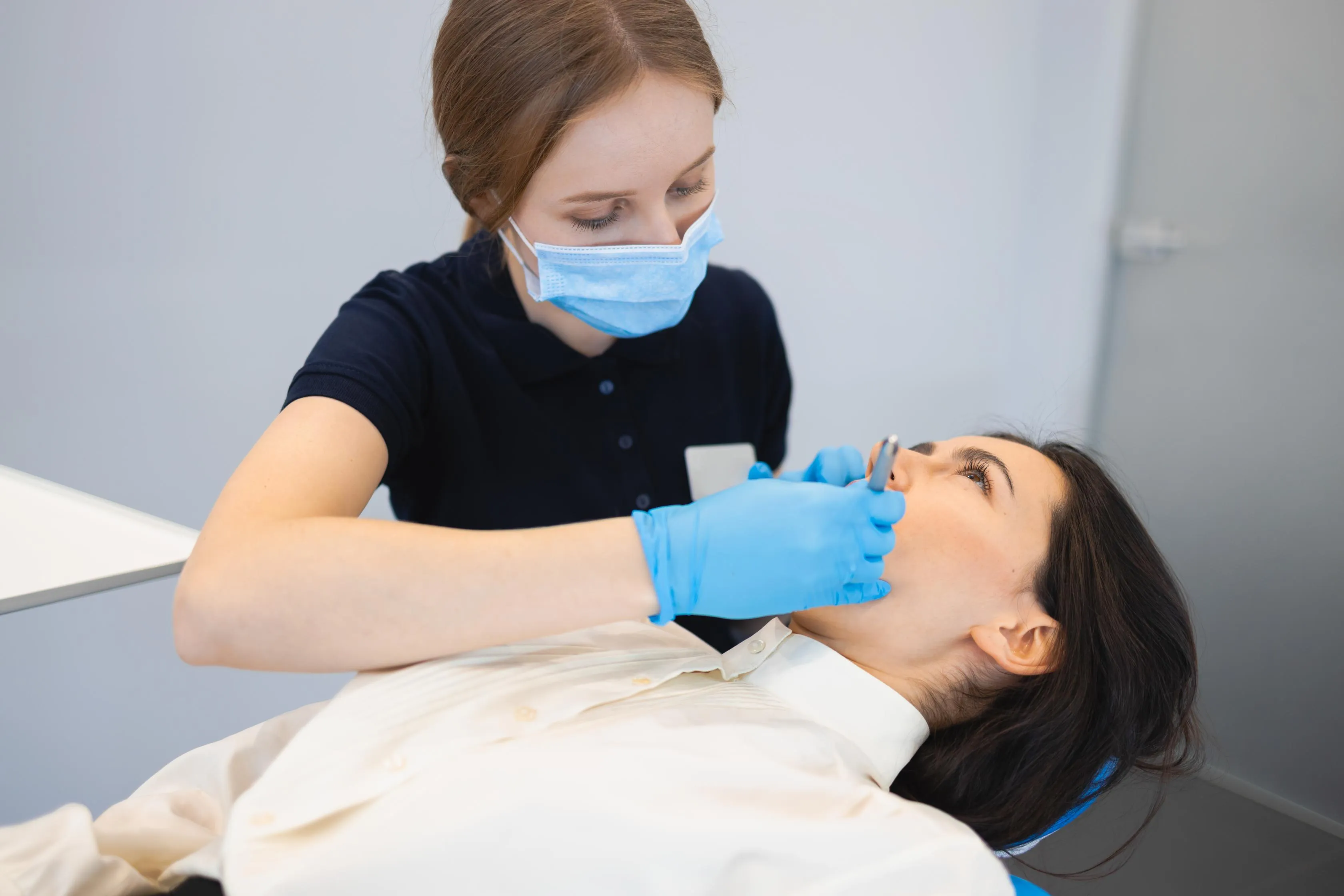 Female dental hygienist in blue gloves examining a patient’s teeth with dental instruments during a routine cleaning and oral health assessment