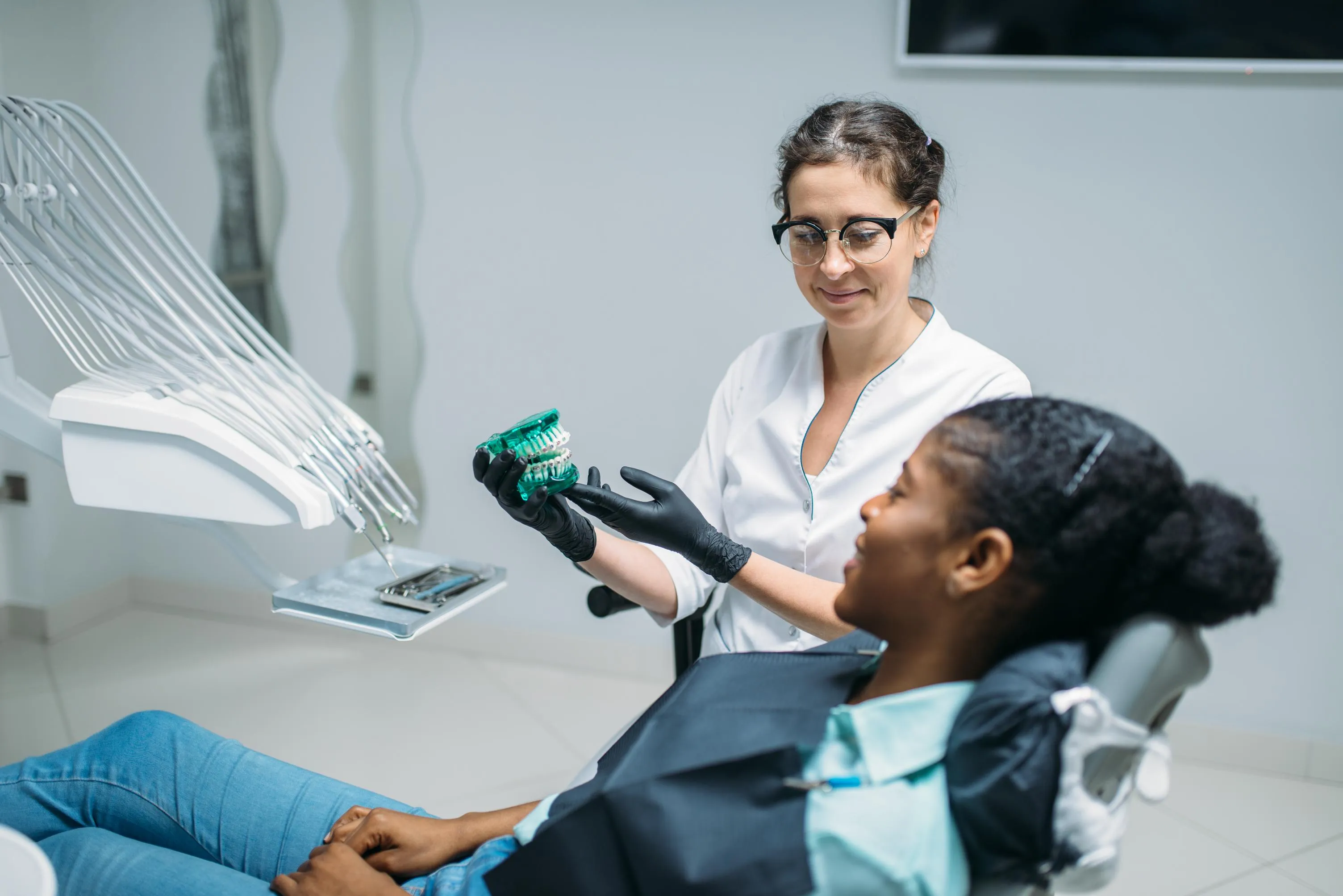 Dentist using a digital X-ray display to explain treatment options to a male patient seated in a dental chair during a diagnostic consultation in a modern dental office