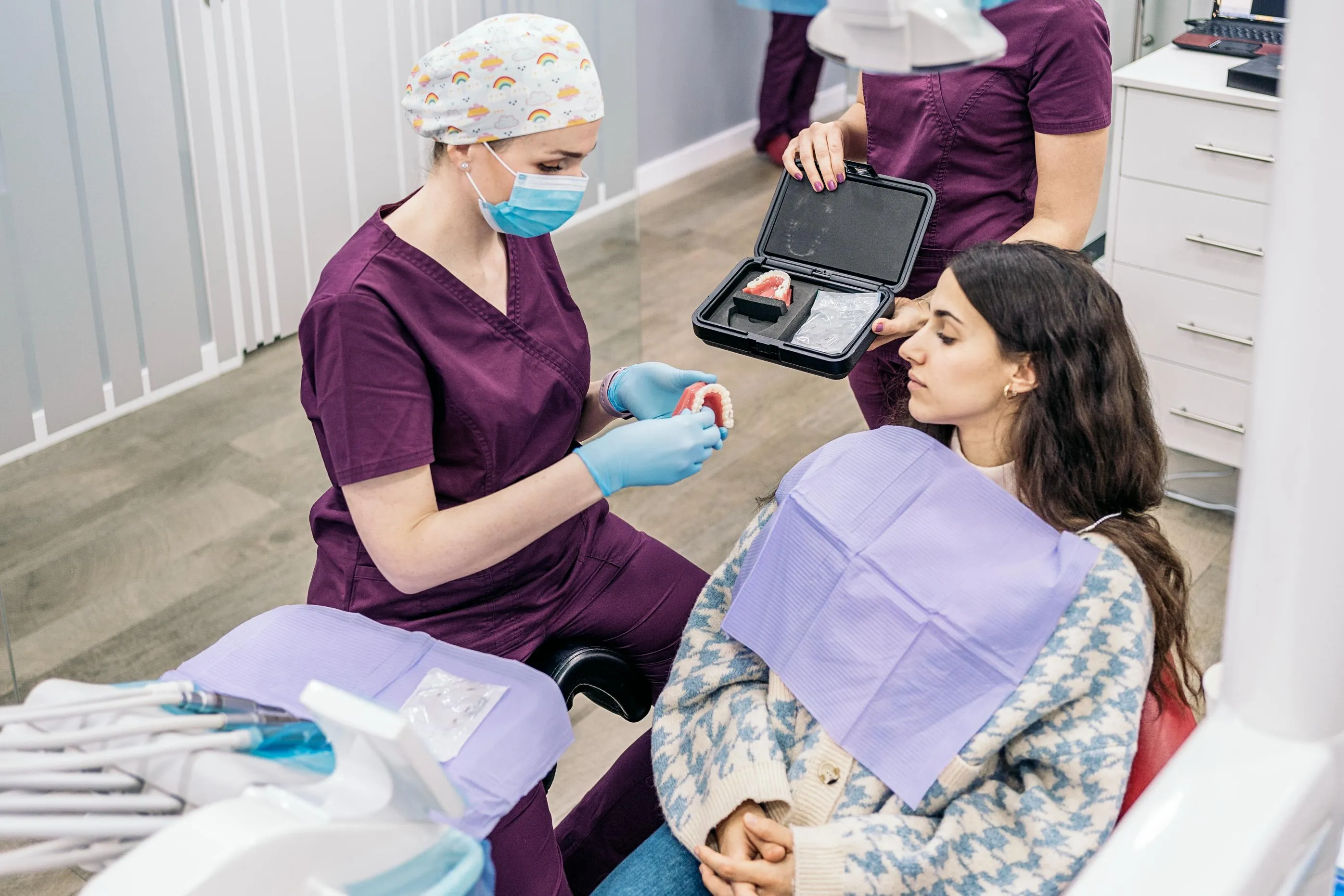 Dental hygienist in purple scrubs performing a professional teeth cleaning for a patient reclined in the dental chair emphasizing preventive oral care and hygiene maintenance