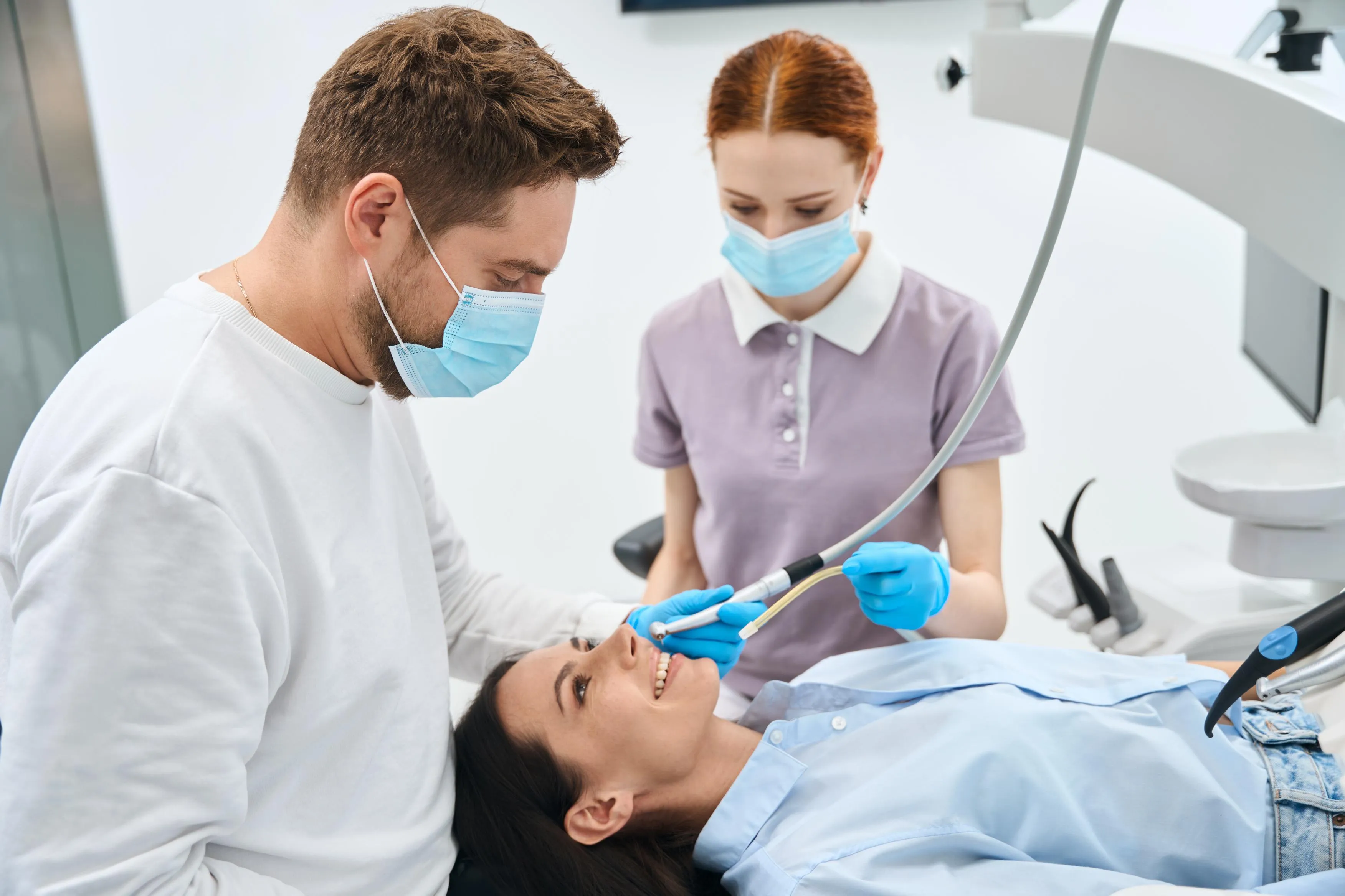 Male dentist wearing protective mask and gloves examining a female patient’s teeth during a professional checkup in a bright, sterile dental office