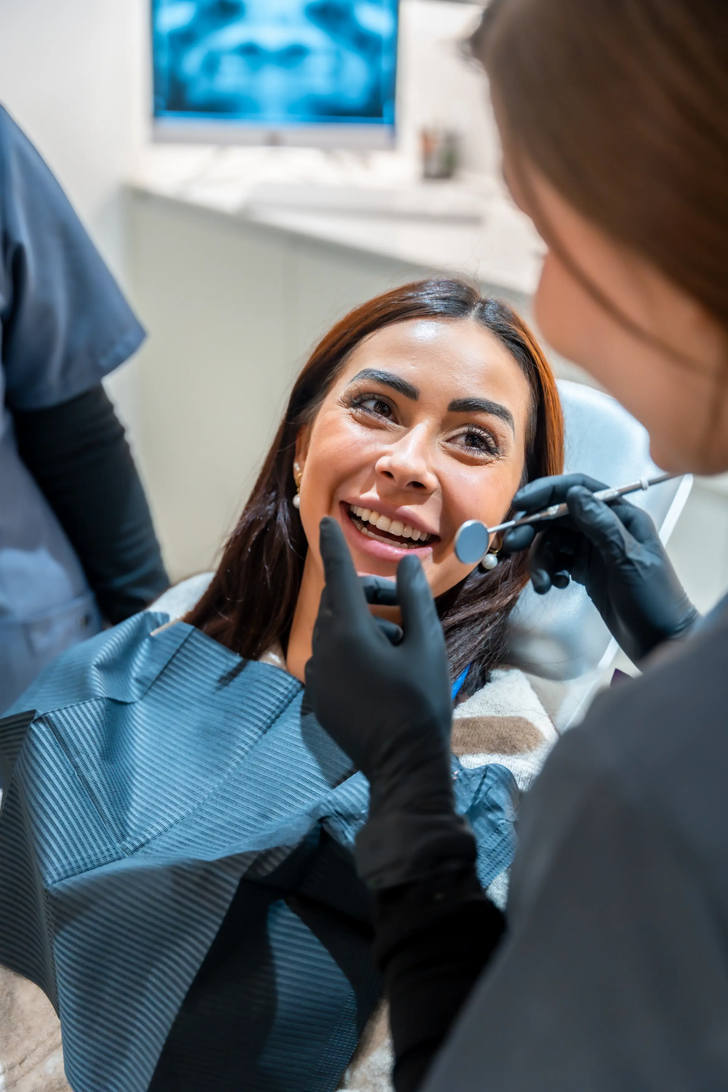 Smiling female dental patient listening attentively to her dentist during a checkup while viewing her dental X-rays on the screen in a bright, modern dental office