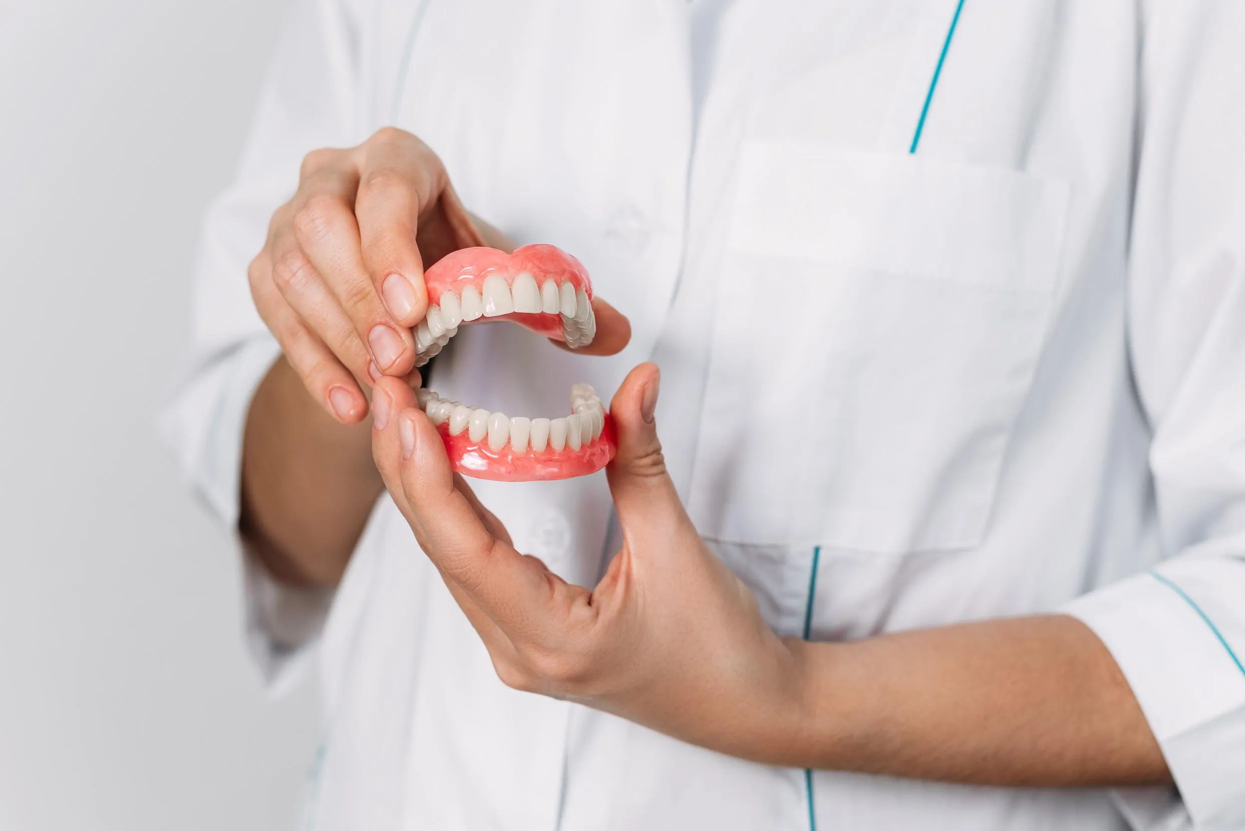 Dentist in a white lab coat holding a full upper and lower denture set while explaining fit, comfort, and cleaning instructions to a patient during a restorative dental consultation