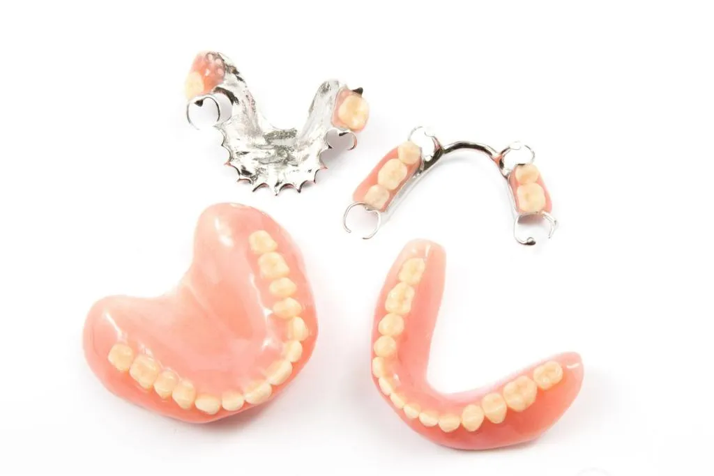 Detailed image showing a variety of full and partial dentures with pink acrylic bases and metal clasps displayed on a white background demonstrating different styles of removable tooth replacement options