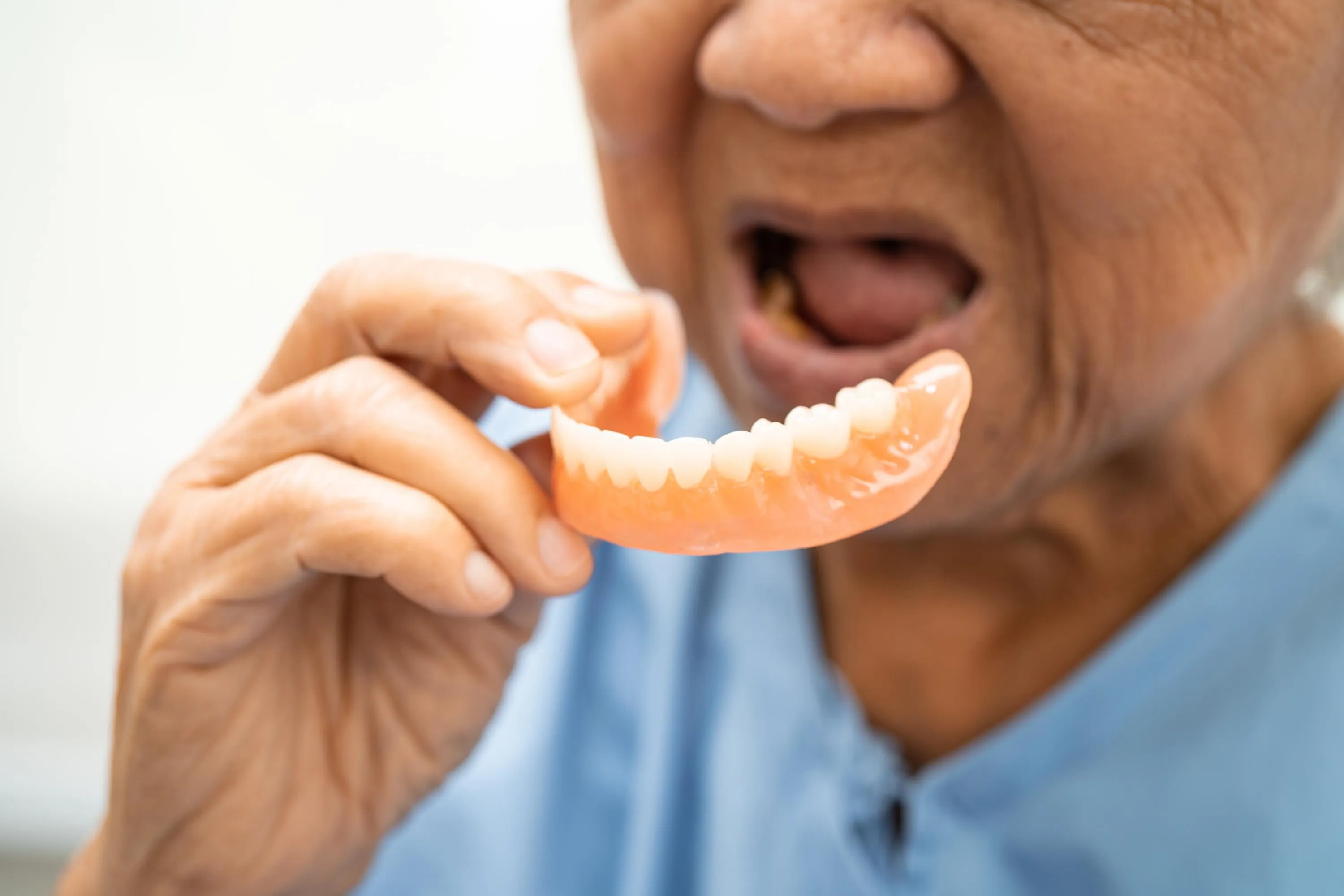 Elderly man inserting his lower dentures while smiling demonstrating the comfort and functionality of custom-fitted dental prosthetics