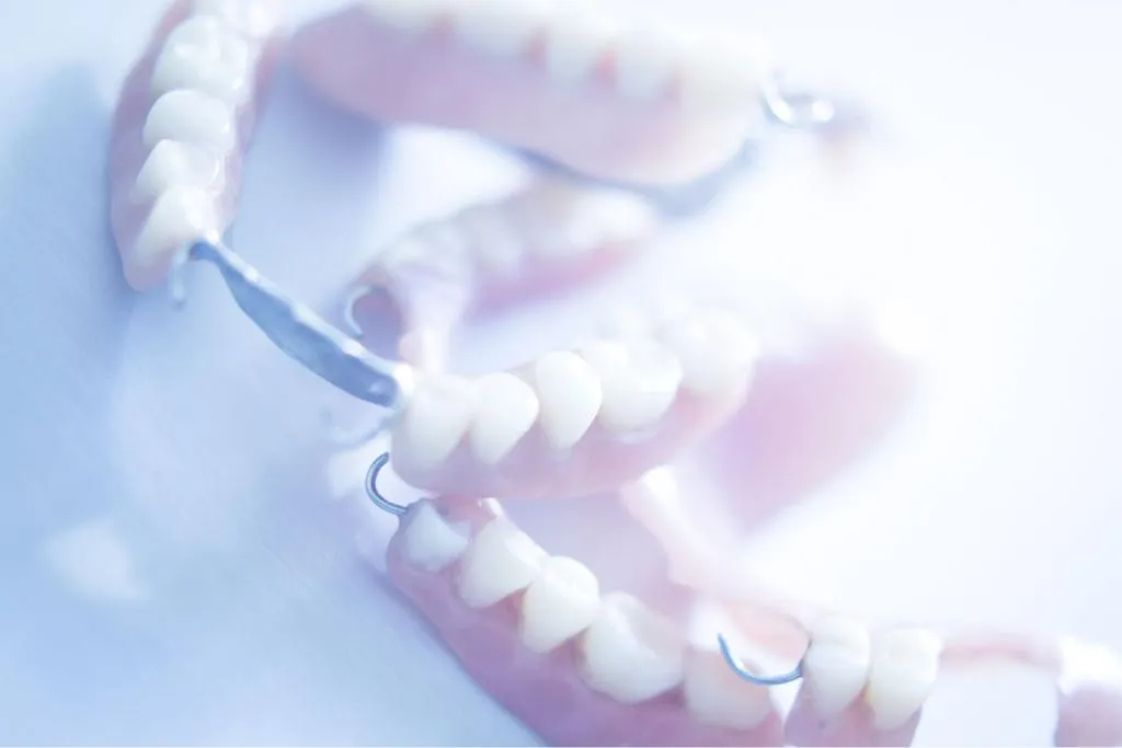 Close-up of removable partial dentures with metal clasps placed on a light blue surface showing realistic tooth design and gum-colored base for natural tooth replacement