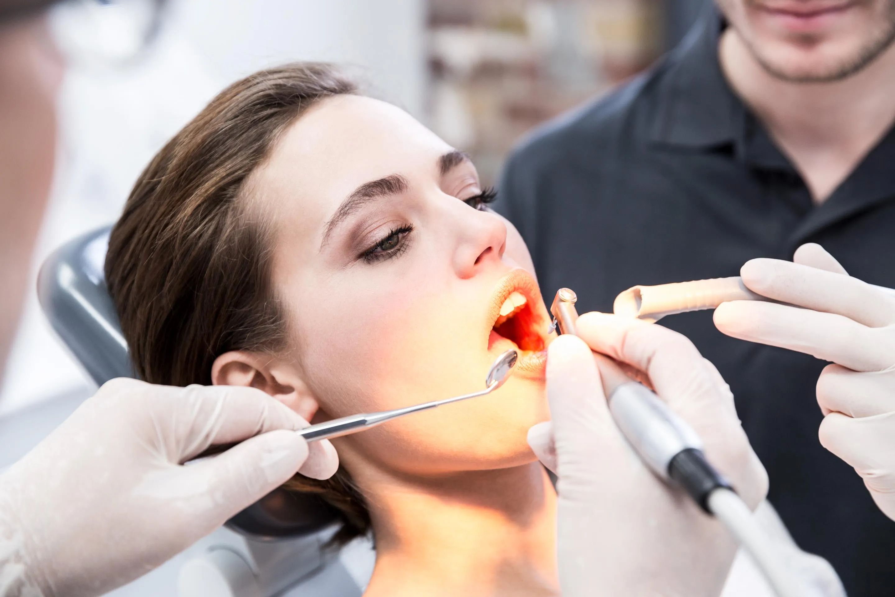 Female patient receiving dental treatment with specialized tools while dentist and assistant perform a procedure in a modern clinic emphasizing professional oral care and precision dentistry