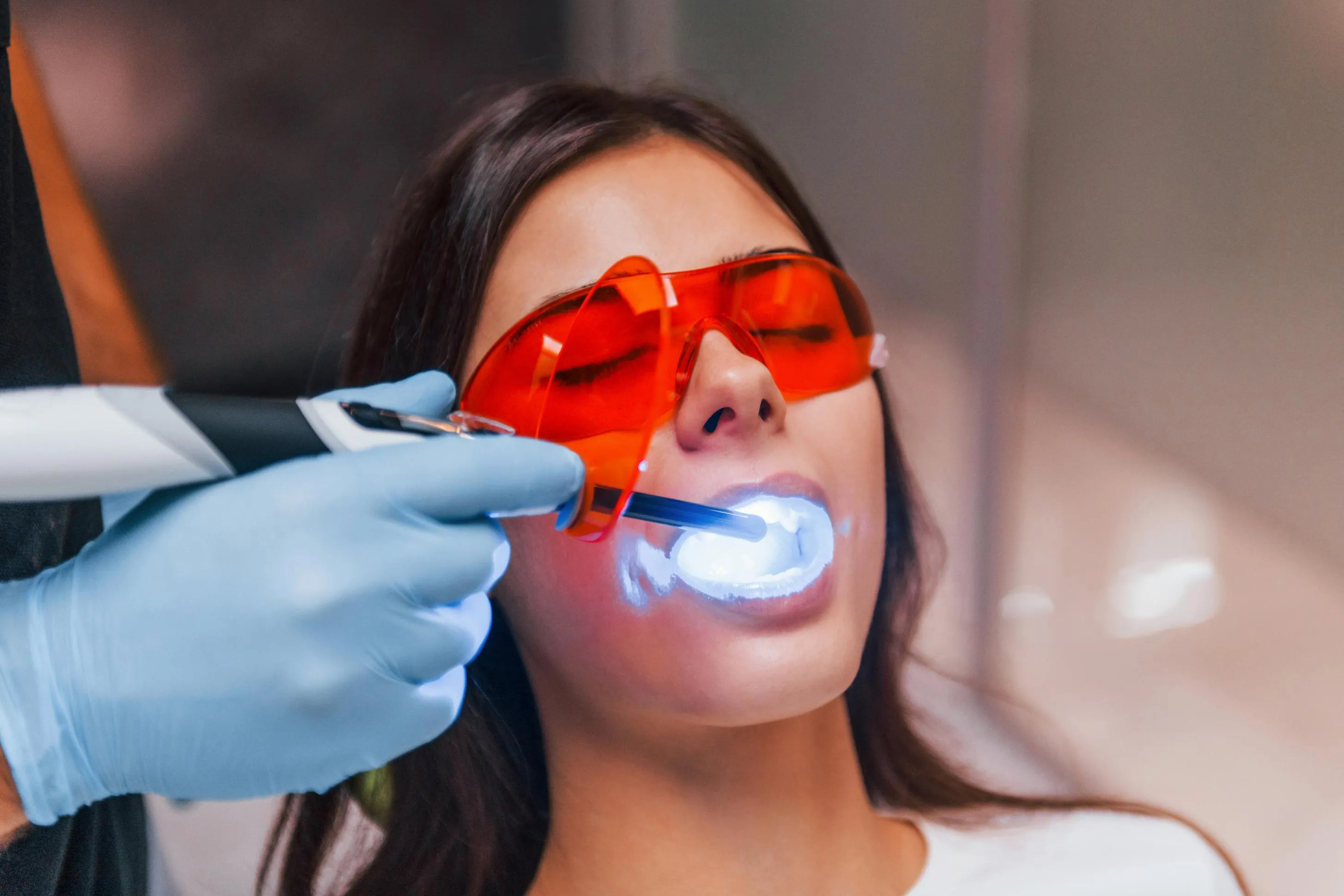 Female patient wearing red protective glasses undergoing an in-office laser teeth whitening procedure performed by a dentist for brighter and healthier-looking teeth