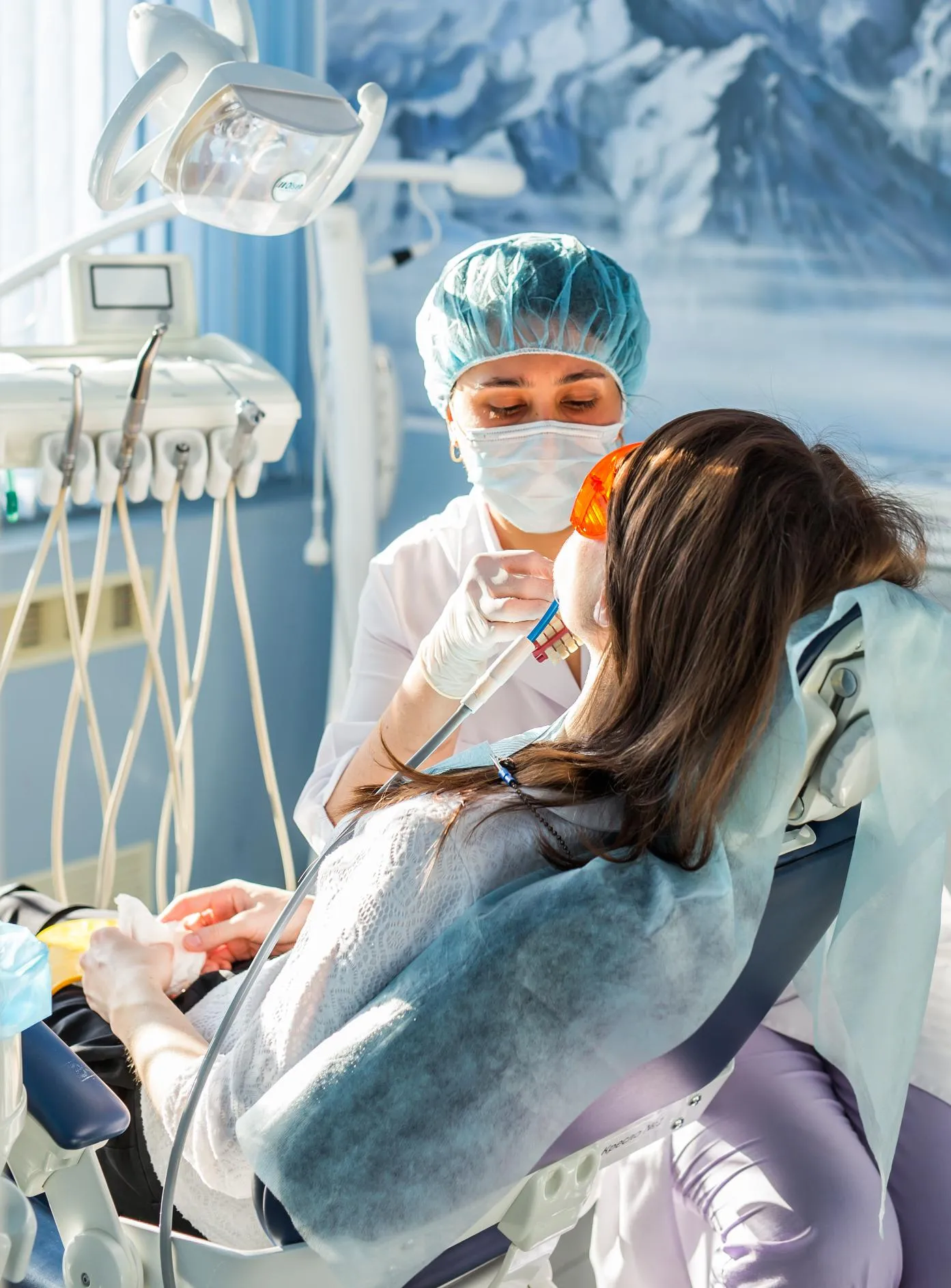 Dentist wearing a surgical mask and cap talking with a female patient during a dental consultation in a bright modern clinic emphasizing personalized dental care and patient communication