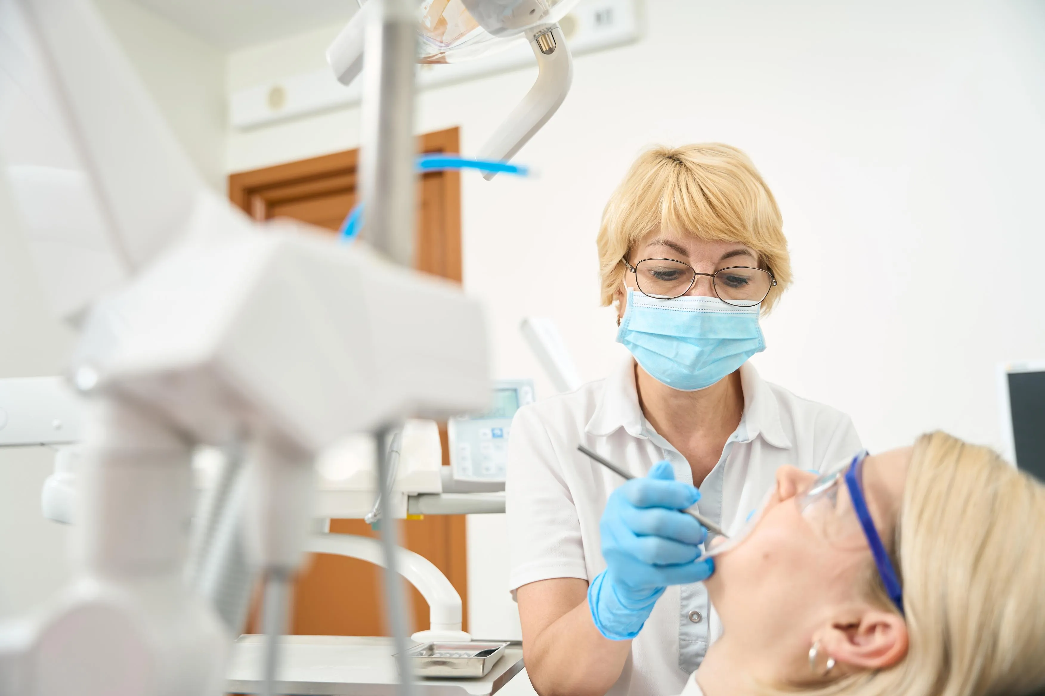 Female dentist wearing gloves and mask treating an adult patient in a modern dental office emphasizing personalized dental care and patient comfort