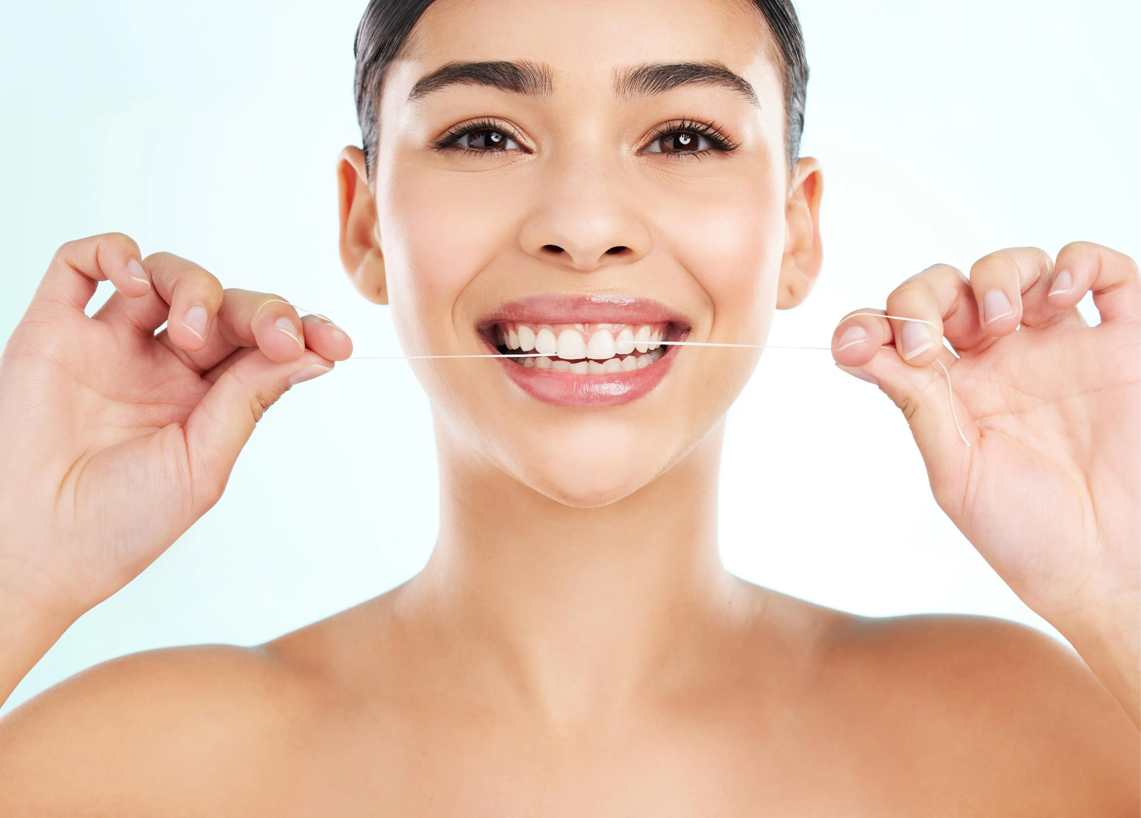 Smiling woman holding dental floss and demonstrating proper flossing technique against a bright background promoting healthy teeth and good oral hygiene practices