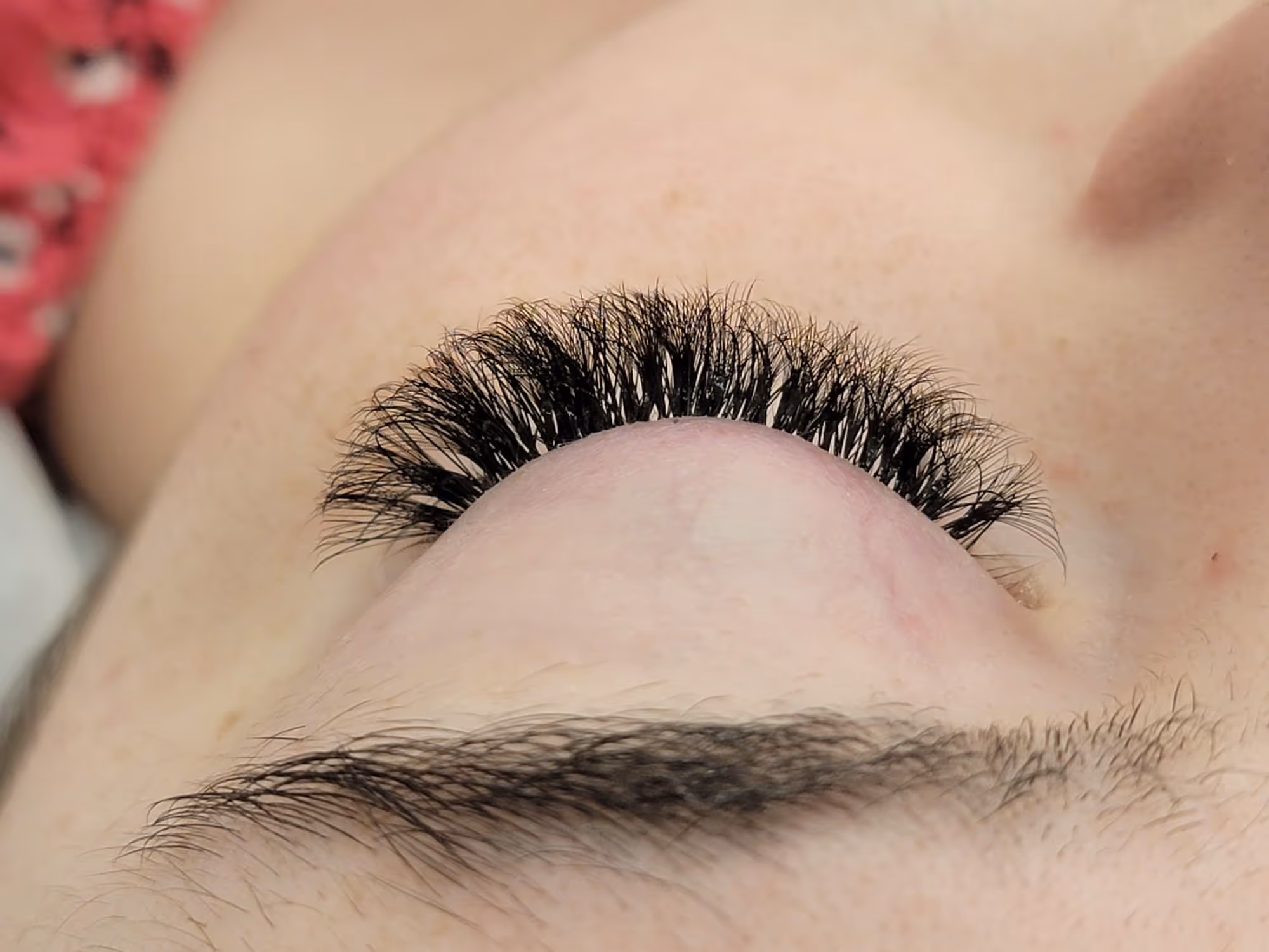 Close-up of a closed eye with long, thick, and curled eyelashes and a natural eyebrow.