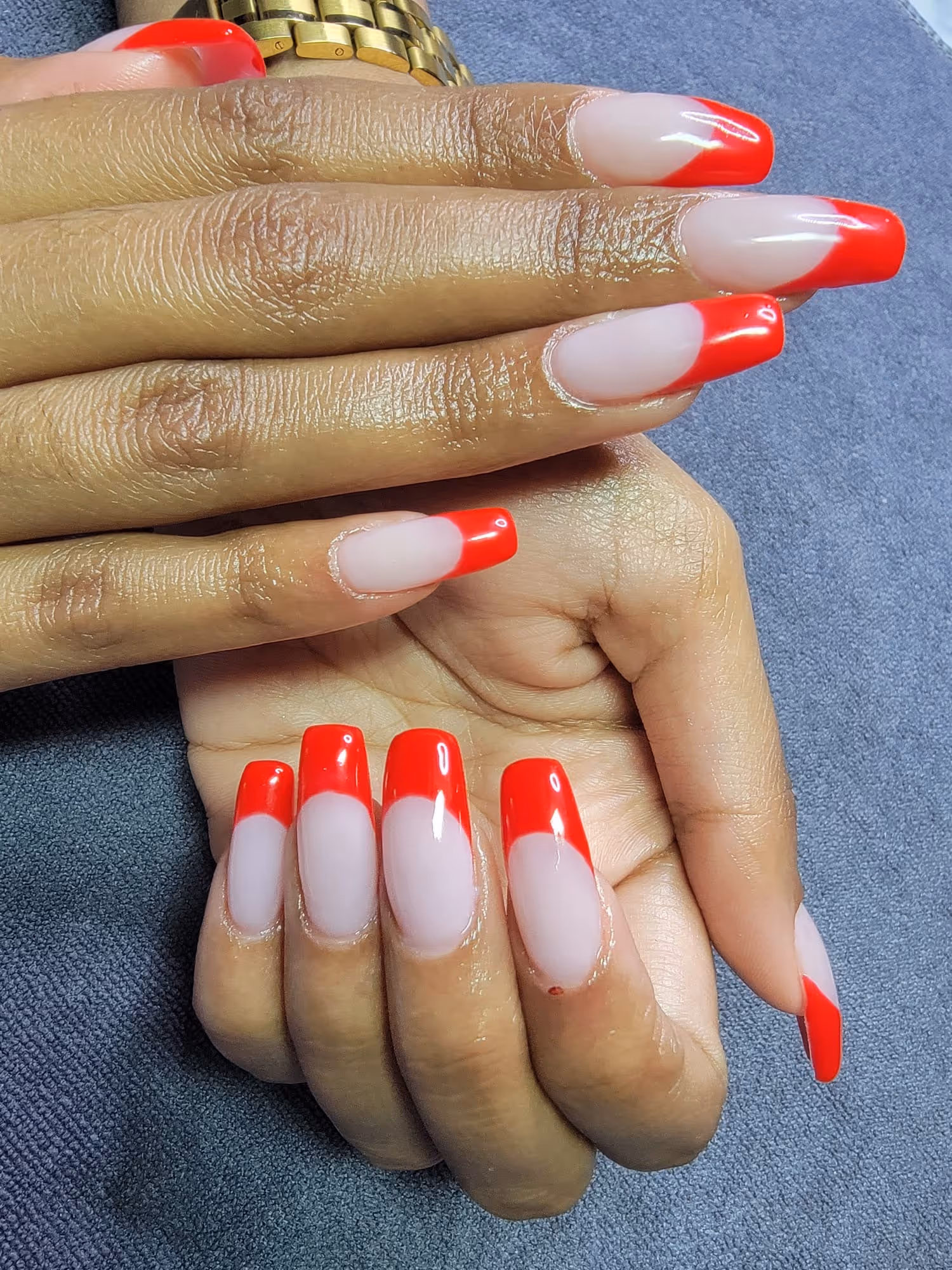 Hands with long coffin-shaped nails featuring a nude base and bright red tips in a half-moon French manicure style.