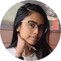 Young woman with long dark hair and glasses resting her chin on her hand, sitting indoors.