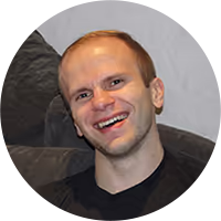 Smiling man with short light brown hair wearing a black shirt, sitting on a dark couch.