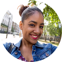 Smiling young woman with a nose ring and denim jacket taking an outdoor selfie on a sunny day.