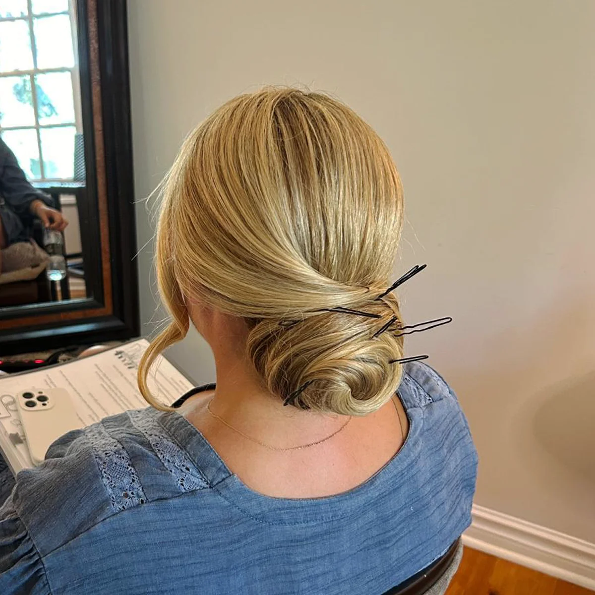 Back view of a blonde woman with her hair styled in a low twisted bun secured with black hairpins.