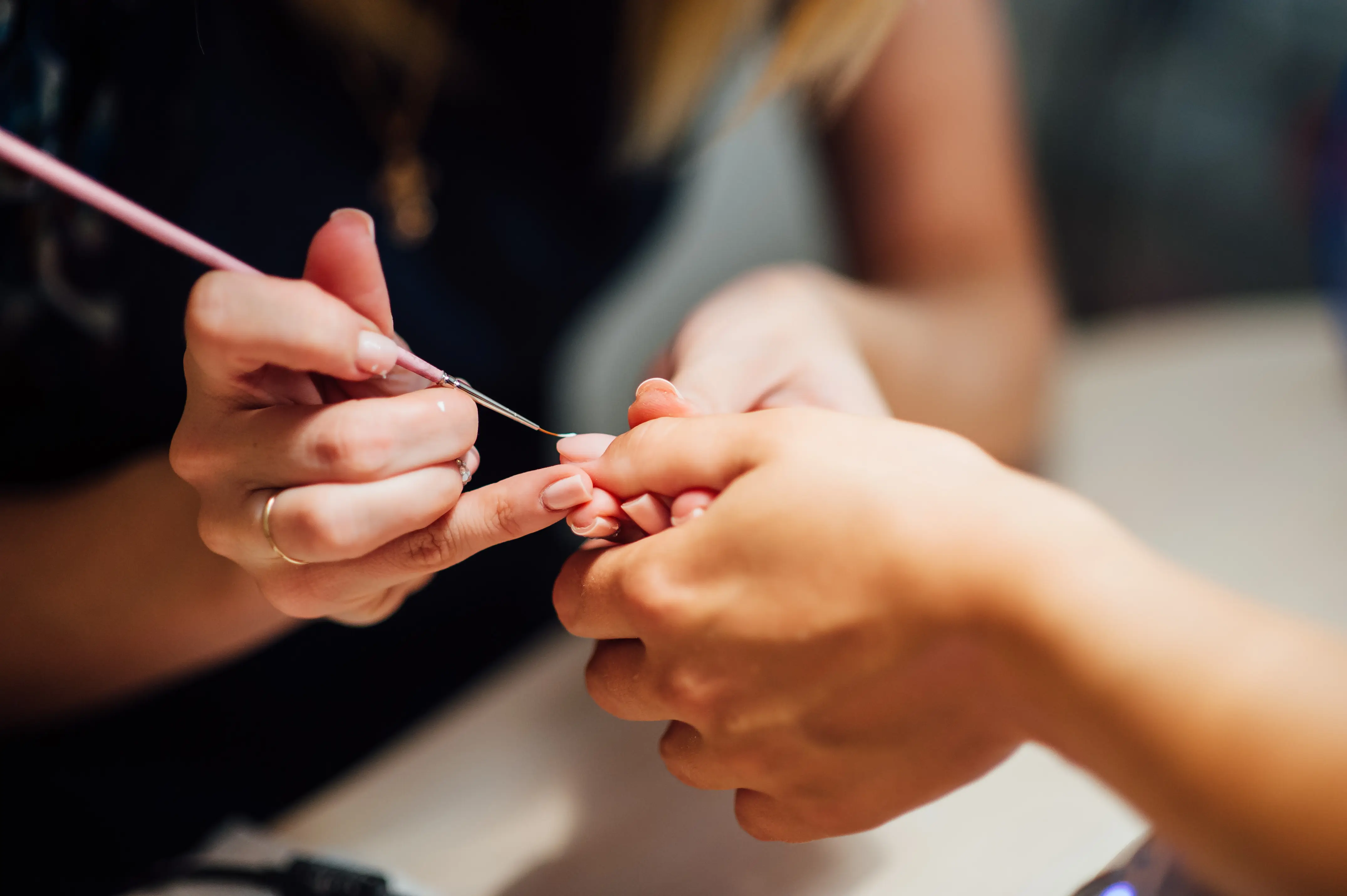 Close-up of a nail technician painting fingernails with a fine brush during a manicure.
