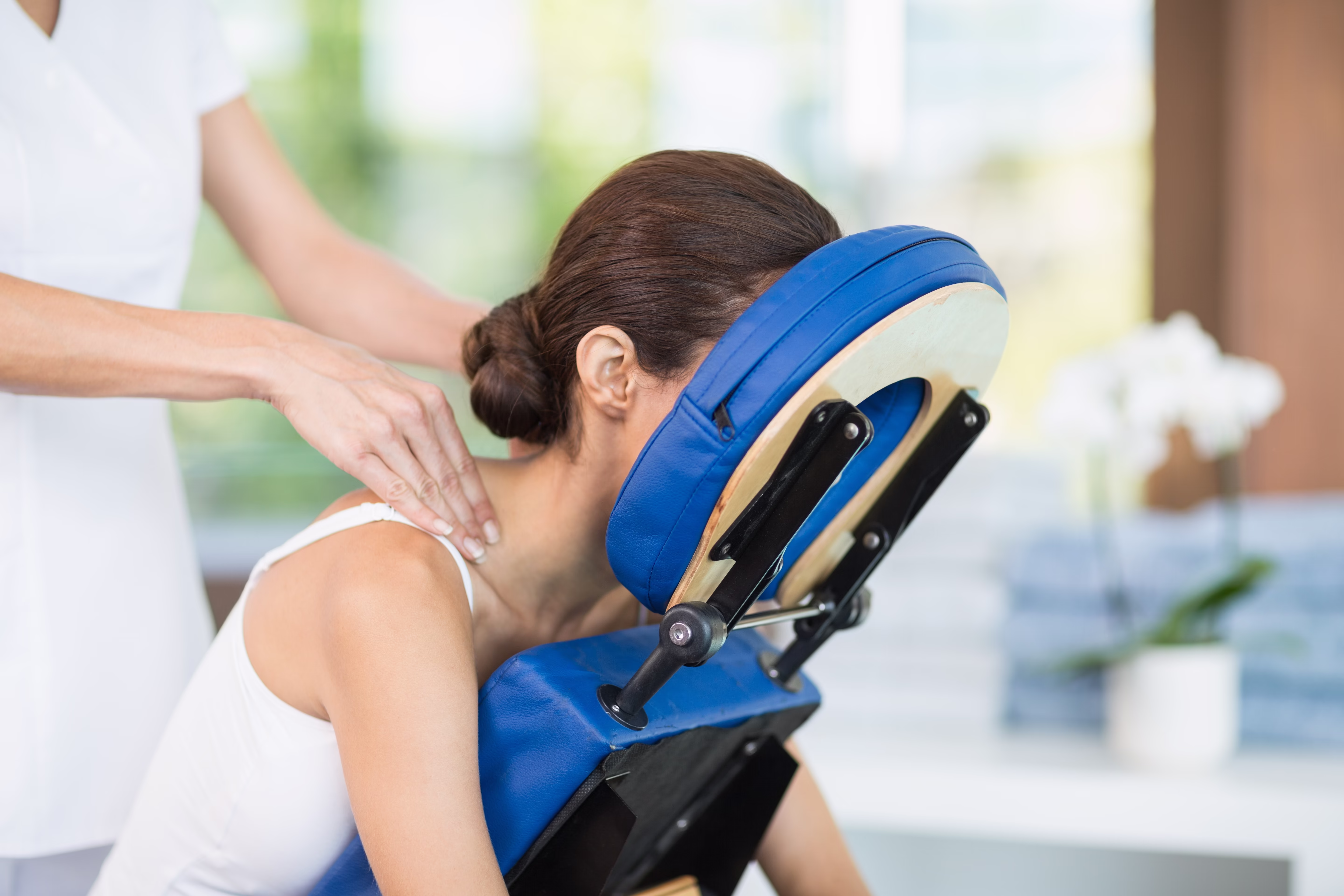 Woman receiving a seated neck and shoulder massage on a blue massage chair.