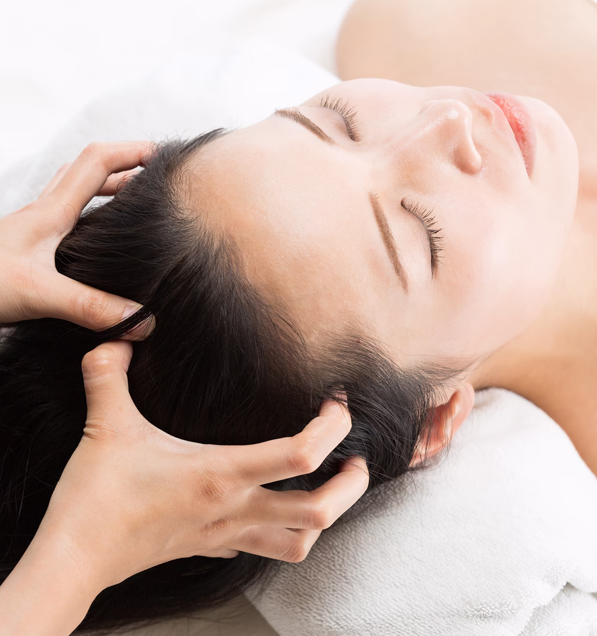 Person receiving a relaxing scalp massage with closed eyes resting on a white towel.