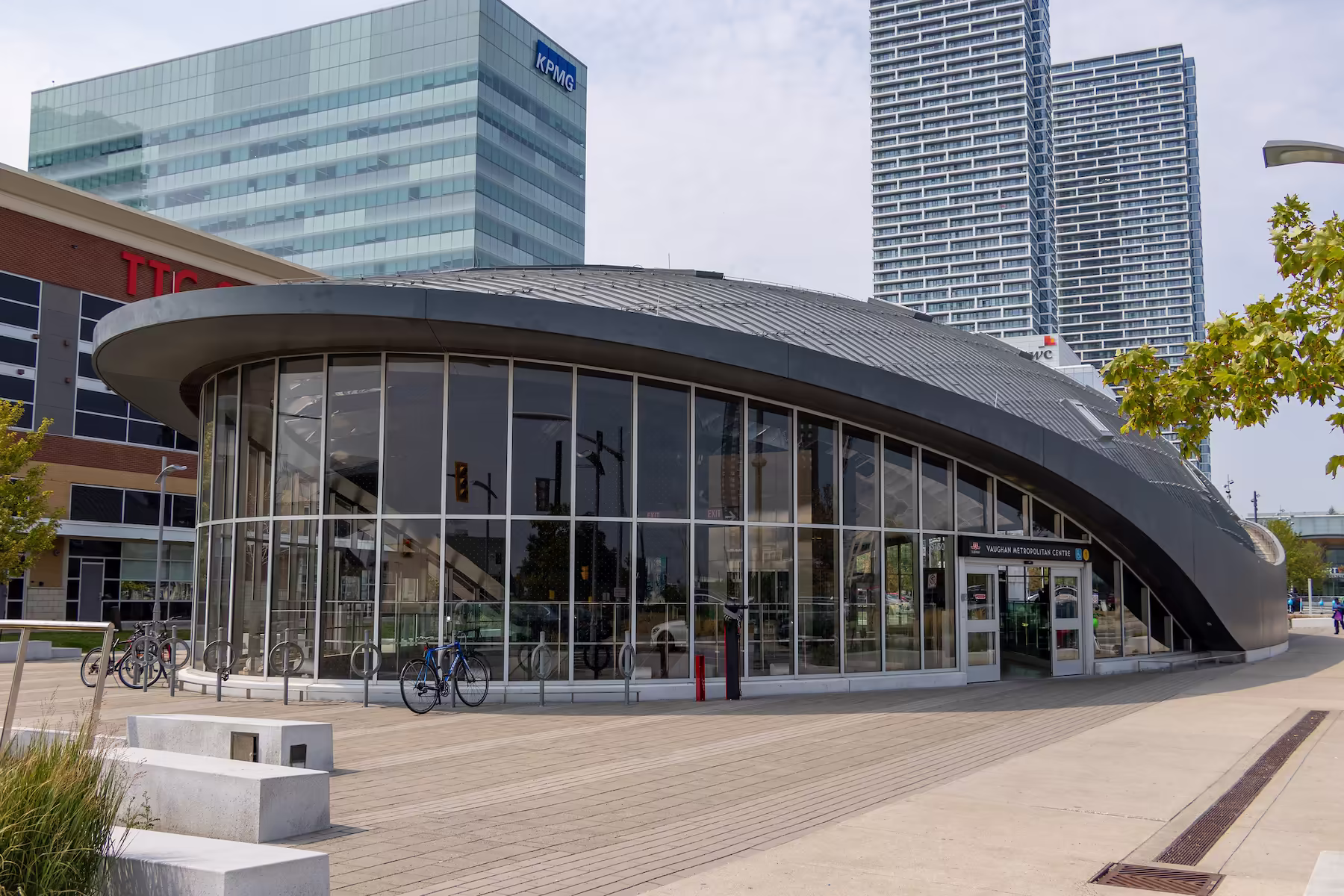 Modern curved glass and metal Vaughan Metropolitan Centre subway station with city buildings in background.