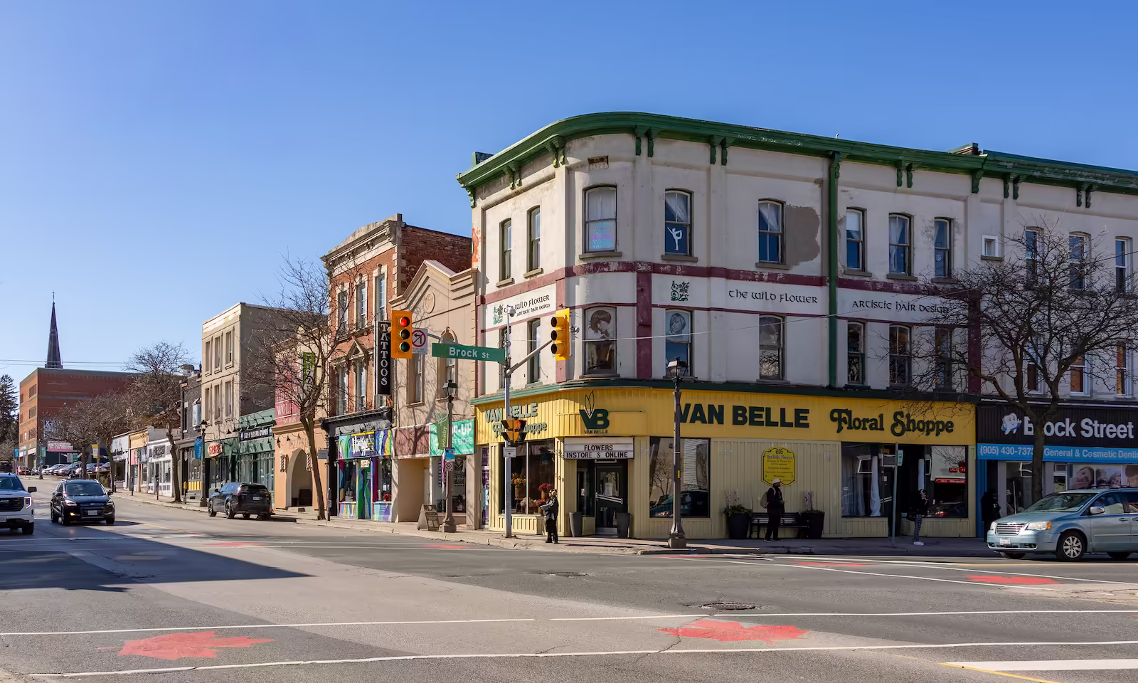 Street corner with shops including Van Belle Floral Shoppe and The Wild Flower hair salon on a clear day.
