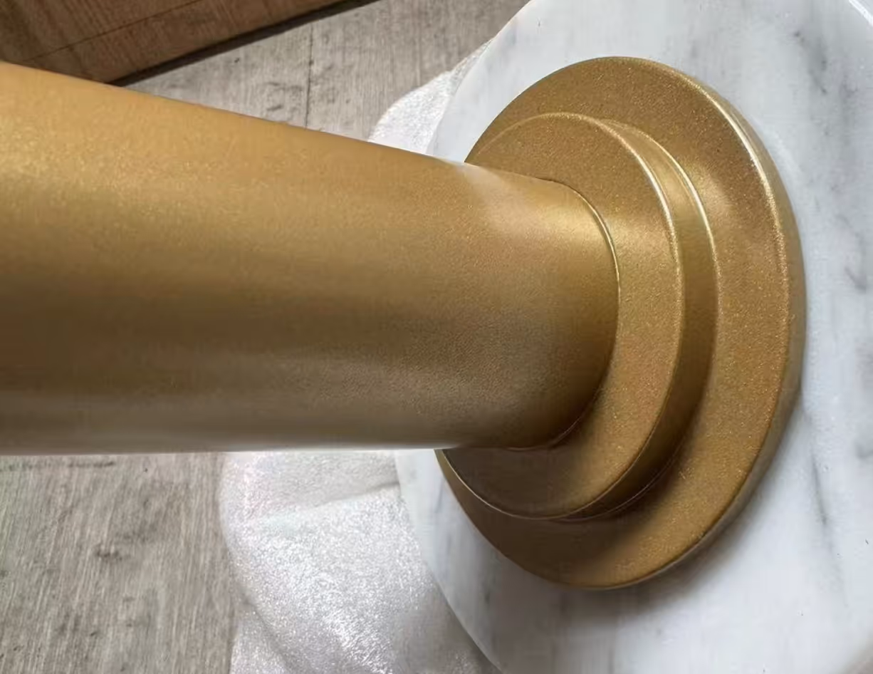 Close-up of a gold-colored cylindrical post attached to a round gold base on a white marble surface.